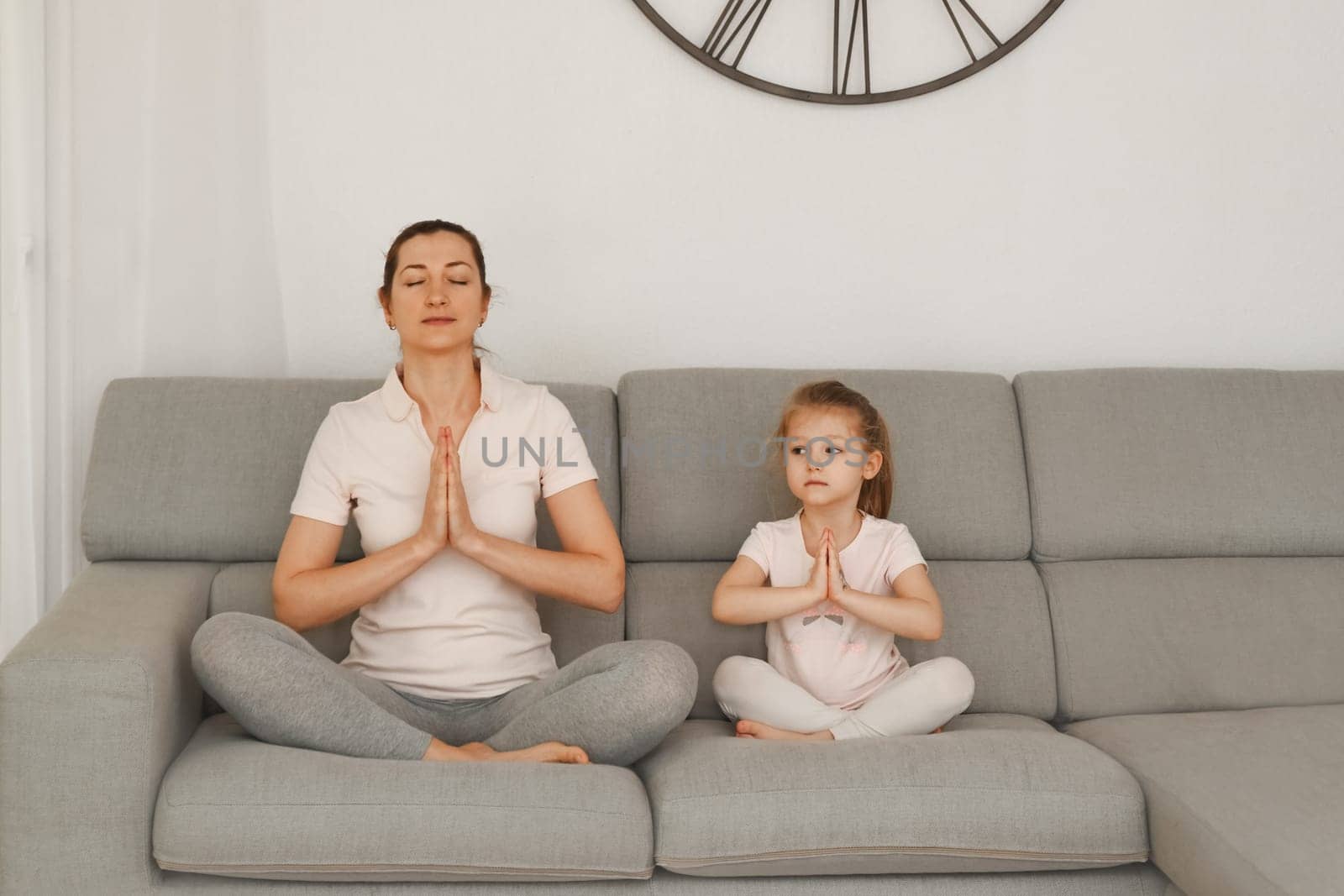 Mother and daughter doing yoga at home. by Godi