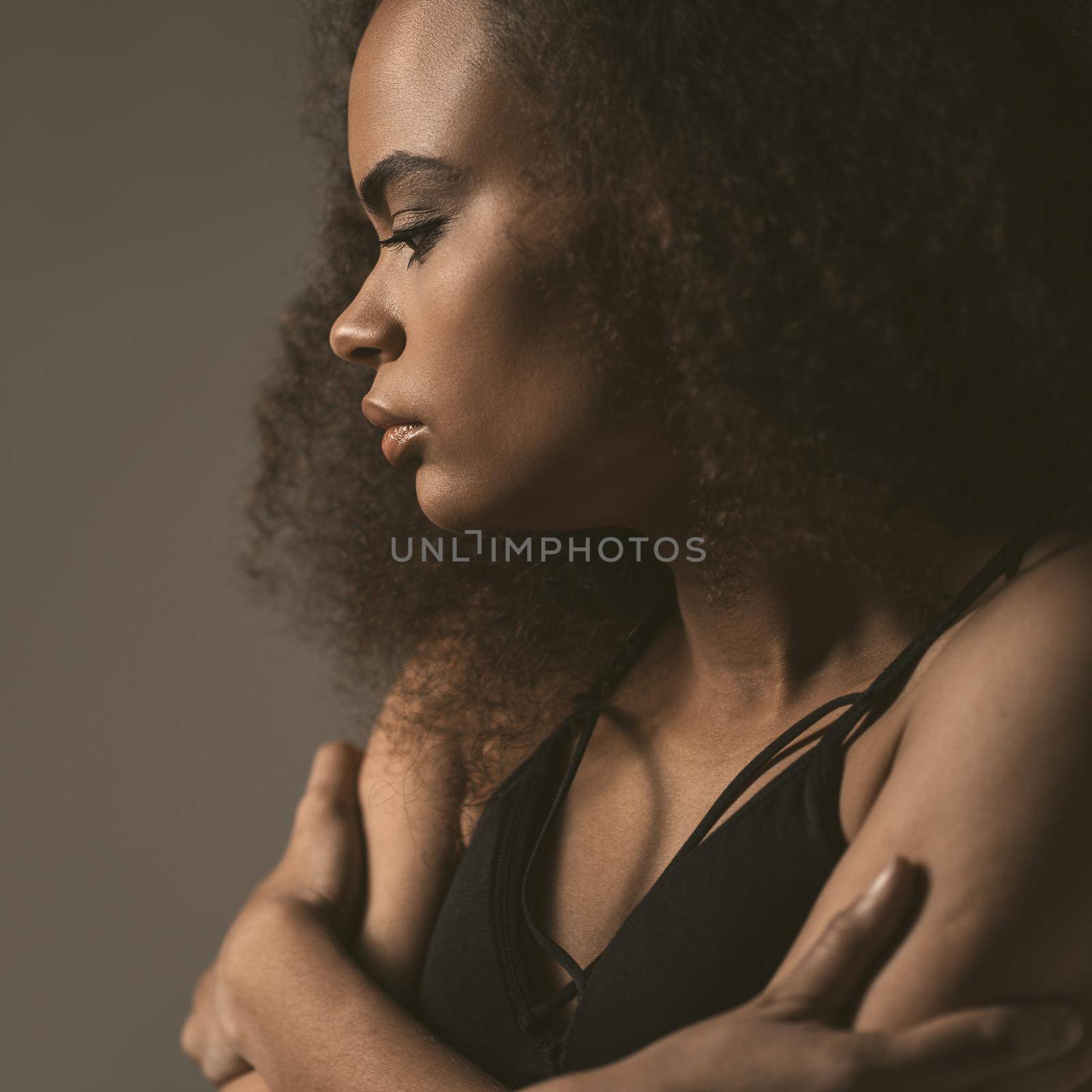Square crop. Standing sideways tender African American girl dressed in black top isolated on grey background. Human emotions, facial expression concept.