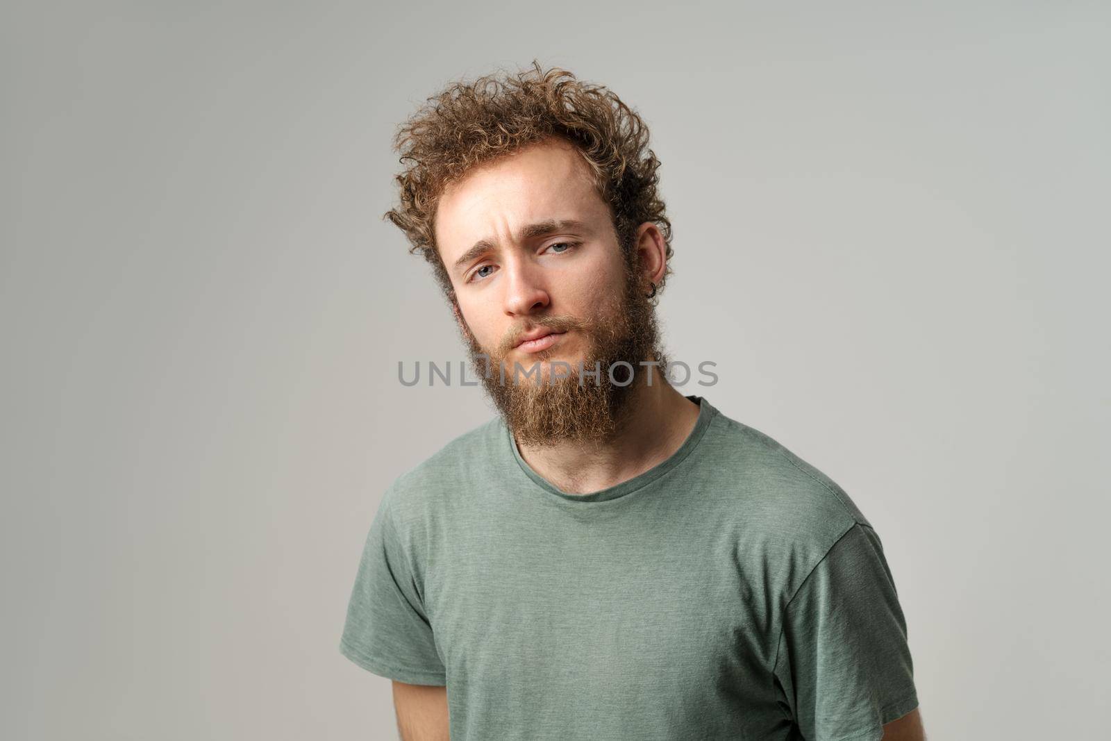 Interrogatively persistent gaze of a handsome young man with curly hair in olive t-shirt isolated on white background. Portrait of smiling young by LipikStockMedia