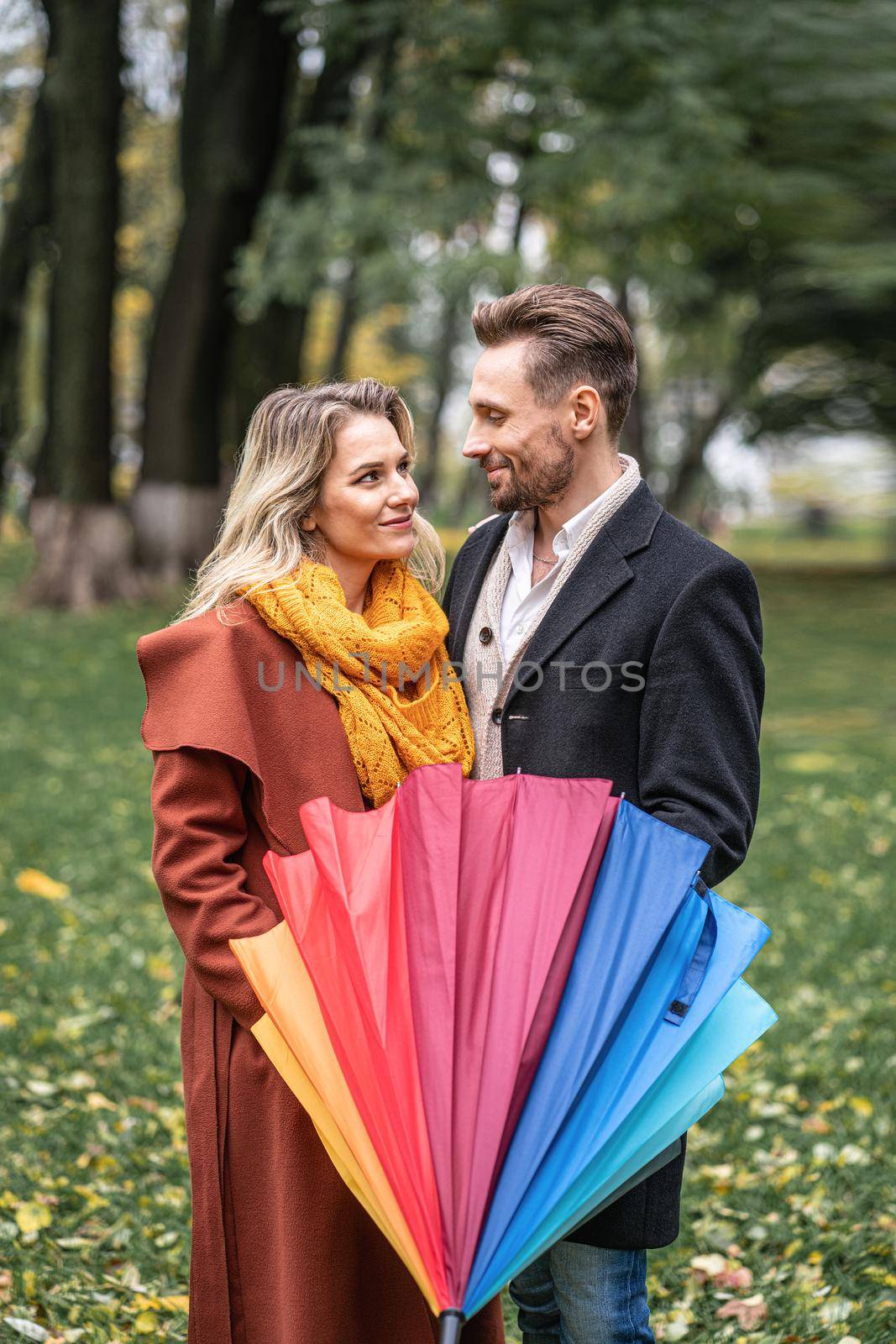 Looking in to the eyes of each other with closed rainbow umbrella beautiful in love couple standing in the park under a. A beautiful couple the autumn park in rainy weather.