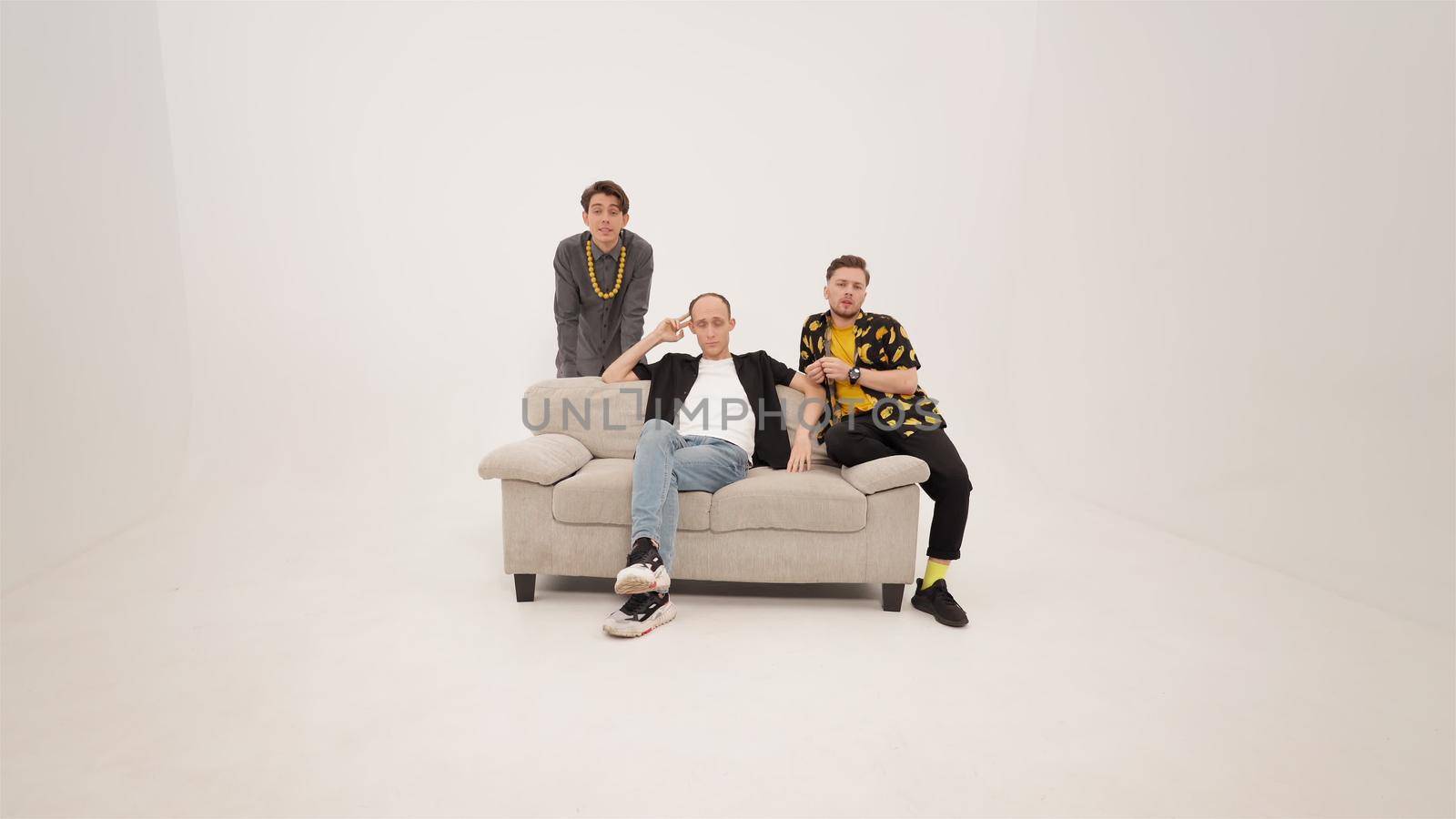 Three stylish young guys sitting on soft couch and talking on the camera. Group of friends are sitting on a soft couch and communicates isolated on white background. 4K footage by LipikStockMedia