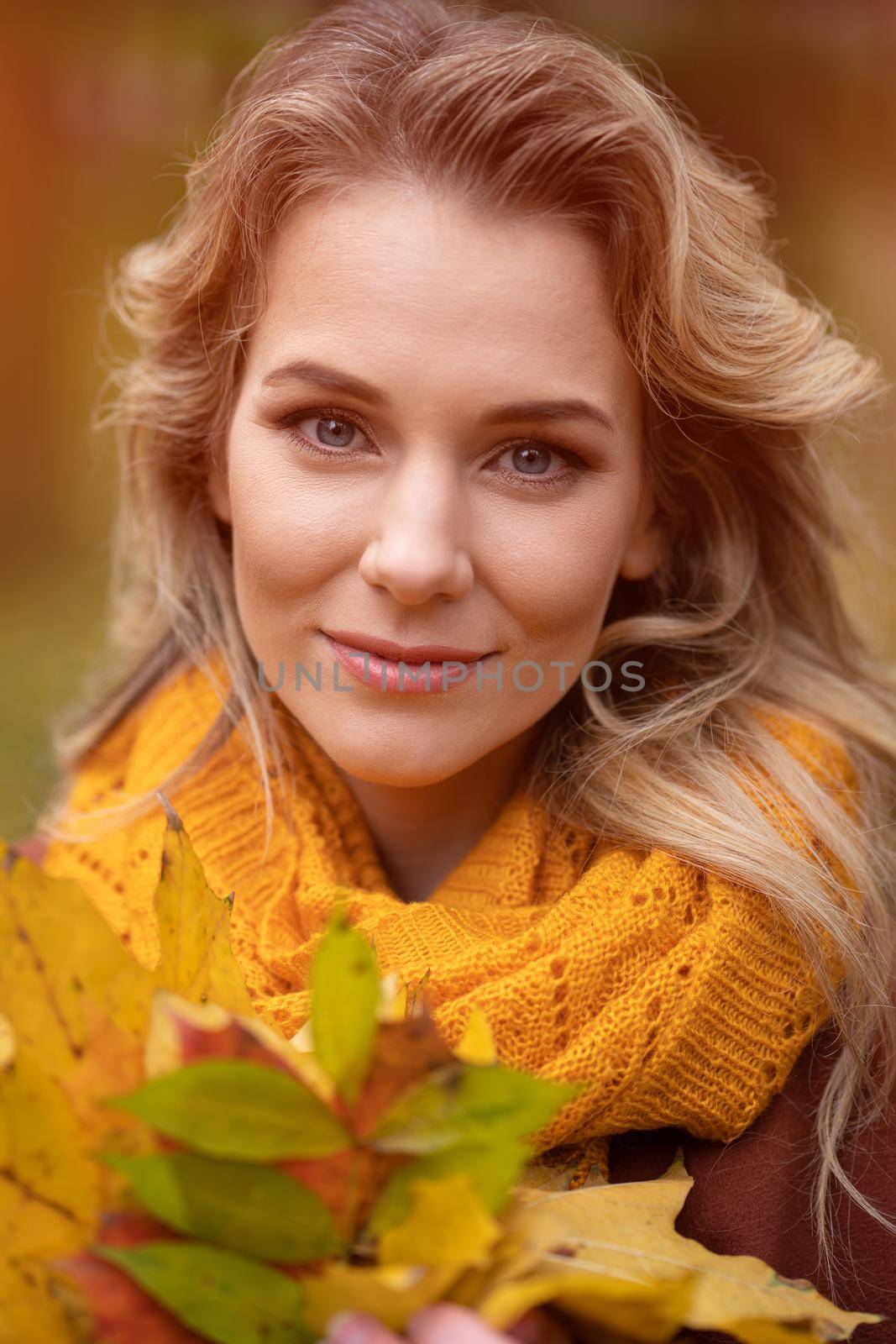Young charming woman posing with fallen yellowed leaves for camera with walking around fall yellow garden or park. Beautiful smiling young woman in autumn leaves.