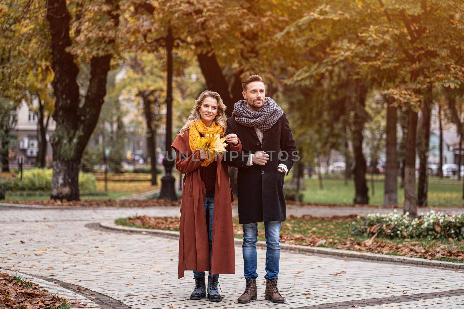 Full length portrait of a couple on a date walking in the autumn park holding hands. Outdoor shot of a young couple in love walking along a path through a autumn park.