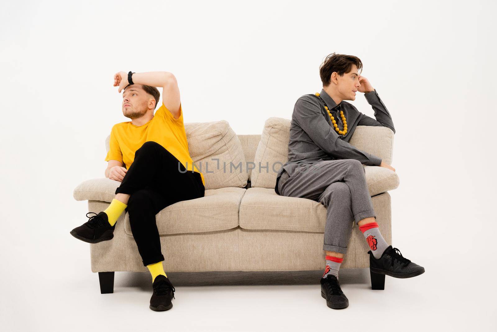 Two handsome guys had a fight while sitting on opposite sides of the sofa. Group of friends are sitting on a soft couch and communicates isolated on white background by LipikStockMedia
