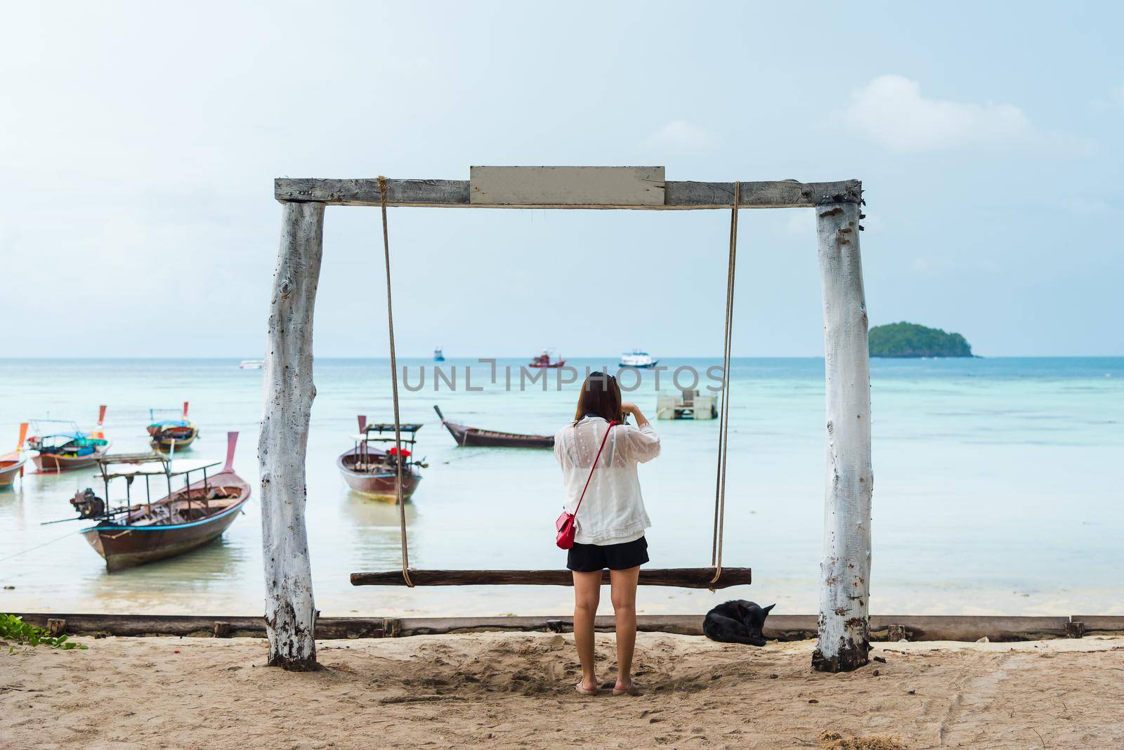 Girl take photo on the swing on the tropical beach by Wmpix
