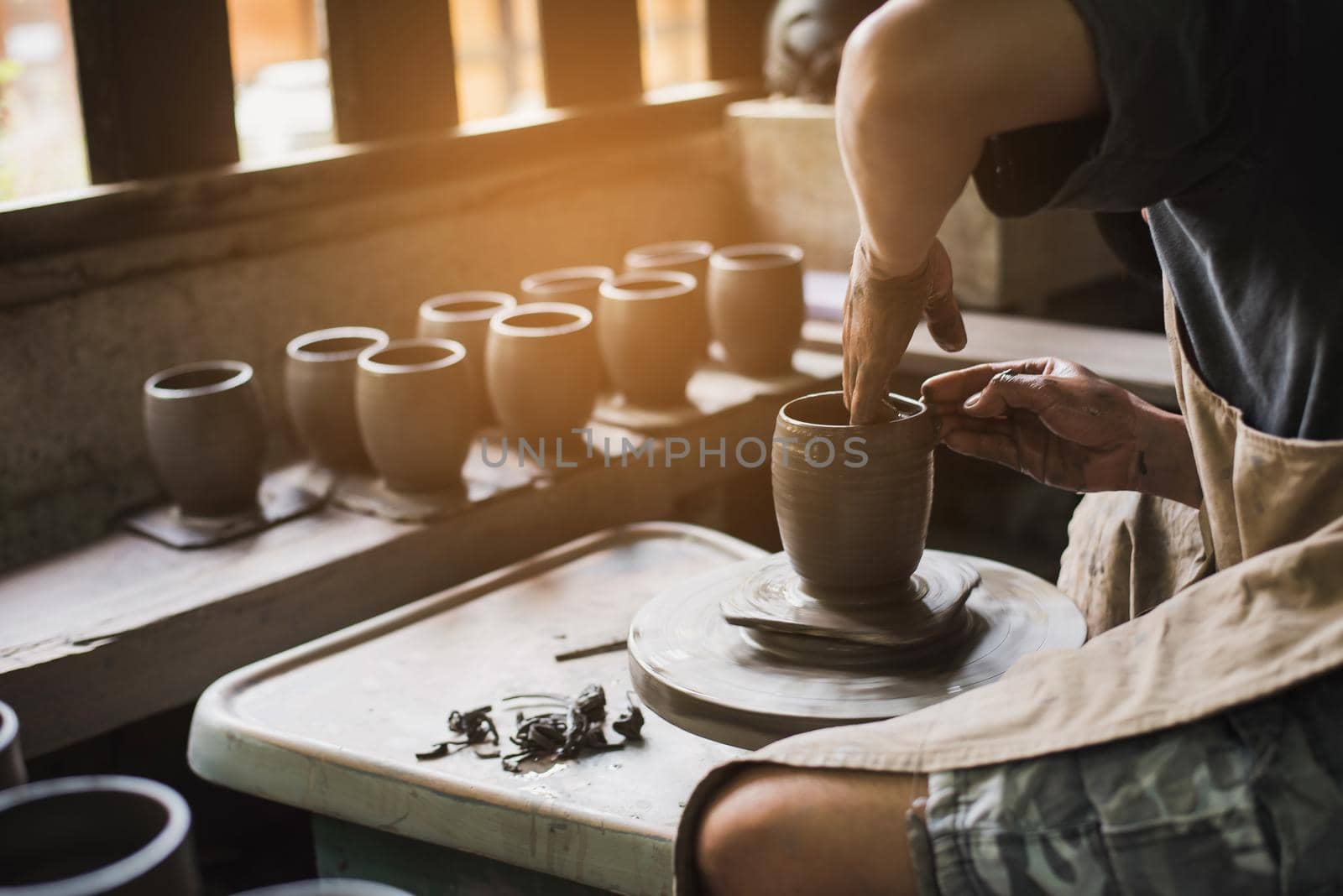 Closeup potter's hands shaping soft clay to make an earthen pot by Wmpix