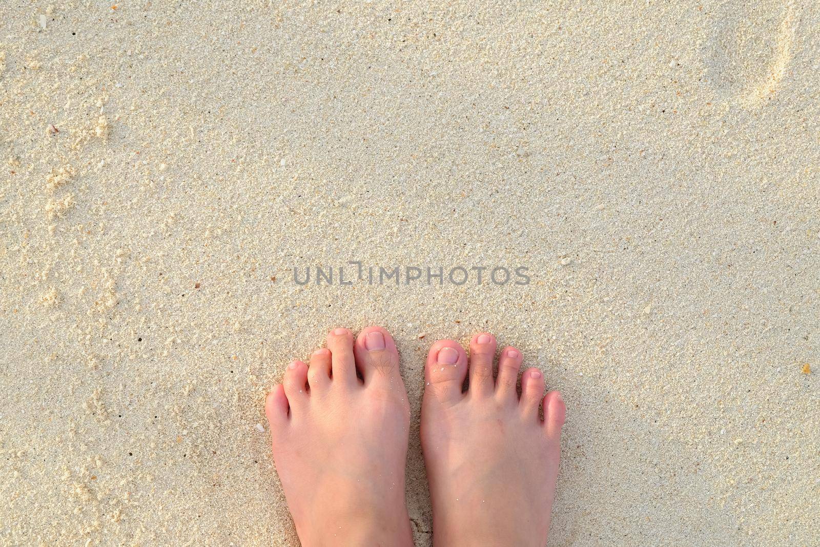 Girl's feet in the sand on the beach by Wmpix