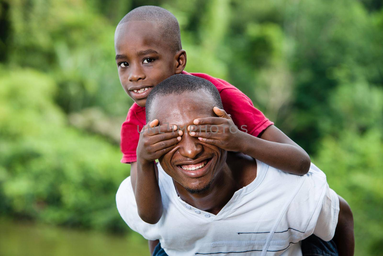 child sitting on his father's neck is holding his eyes closed.Happy young father and son having fun and enjoying the fresh air in nature.