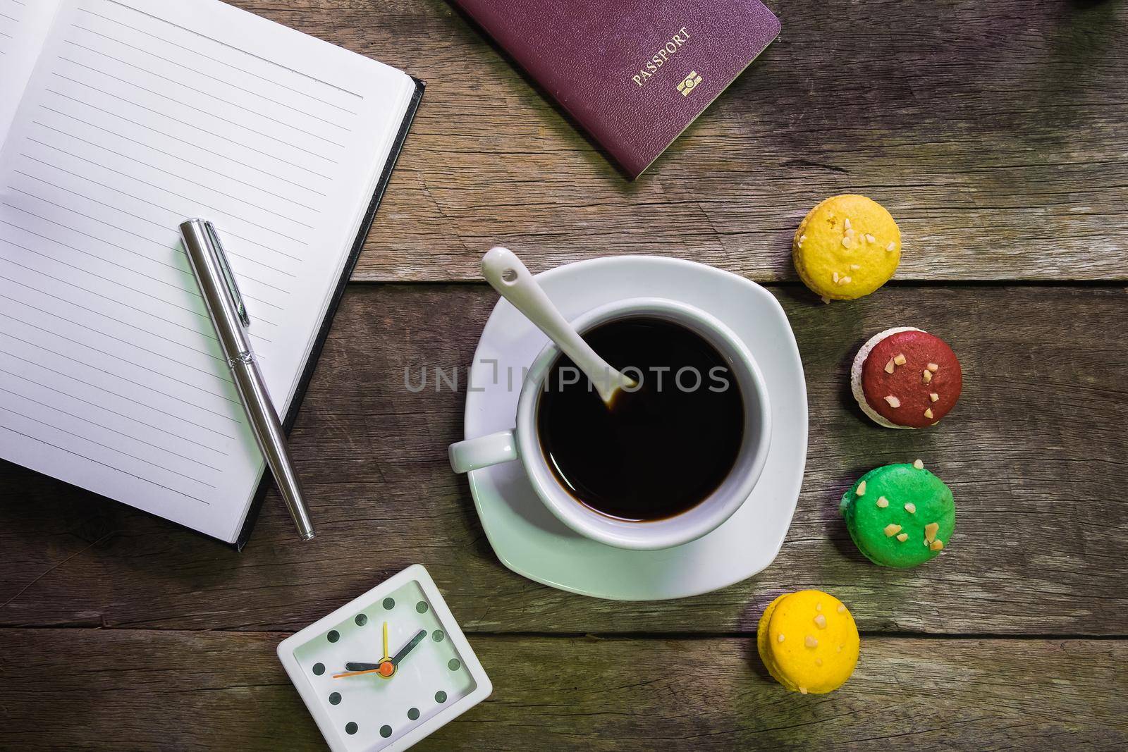 notebook on rustic wood with macaroon and cup of coffee and passport and clock