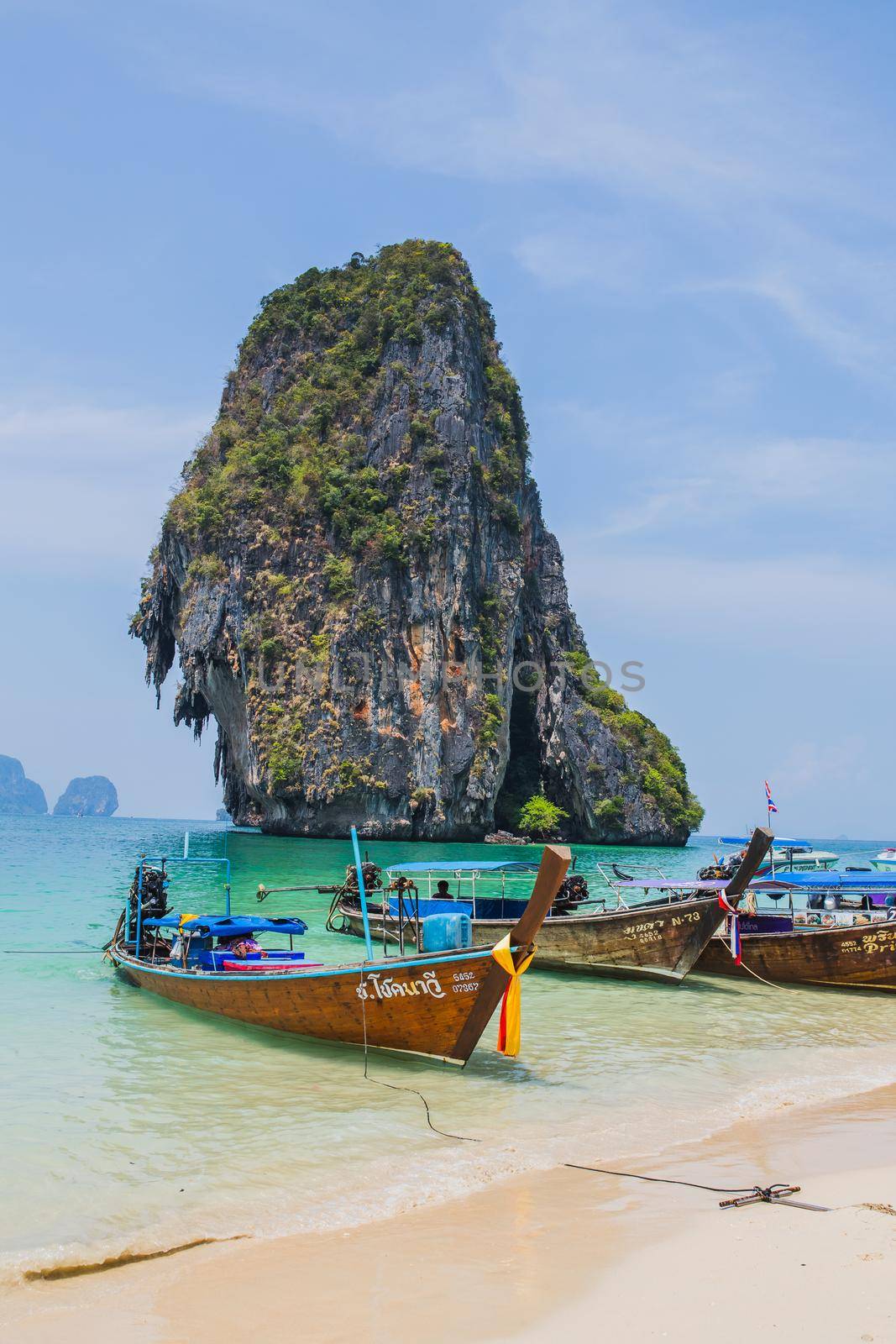 MAYA BAY, THAILAND - APRIL 14, 2014: Dramatic karst geography stands tall above traditional Thai longtail boats docked in the popular Maya Bay. by Wmpix