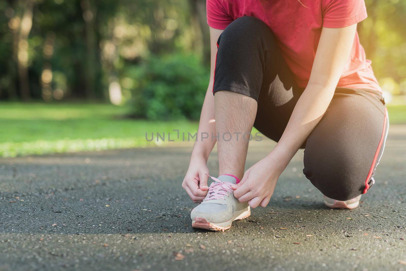 Woman tying her sport shoes in the park by Wmpix