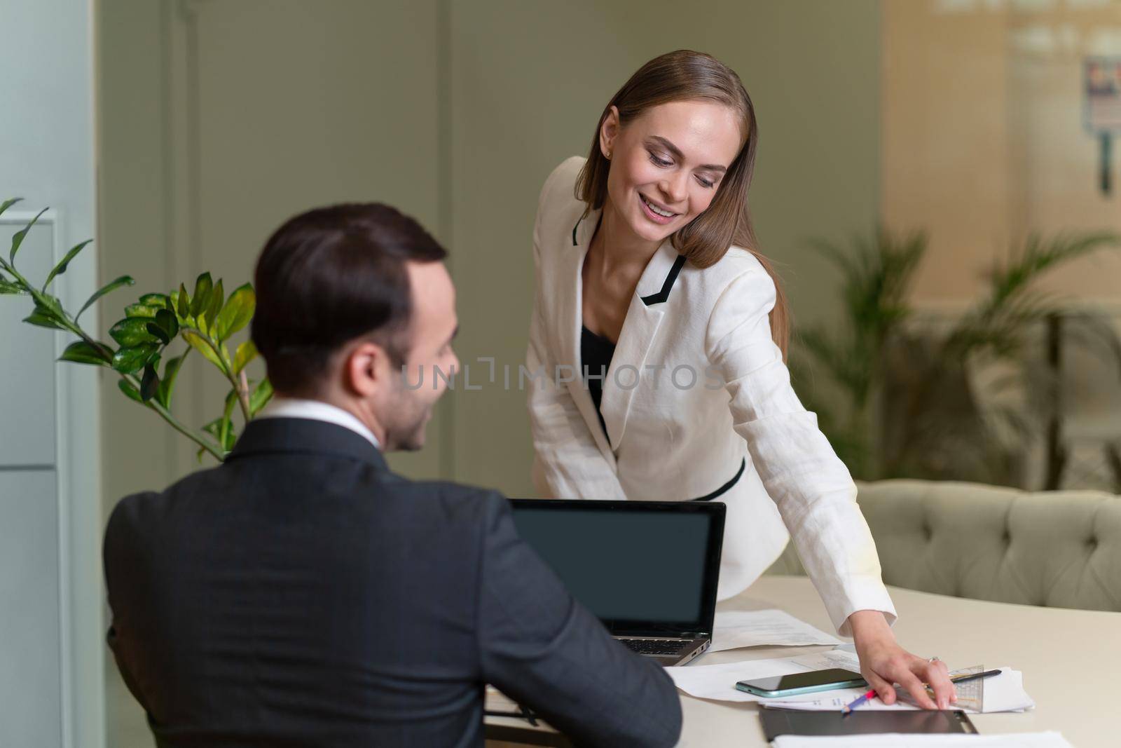 Two young and attractive colleagues man and woman flirting at office. Young woman sitting on the table and sexually leaned toward young man. Flirting in the workplace. Office romance by LipikStockMedia