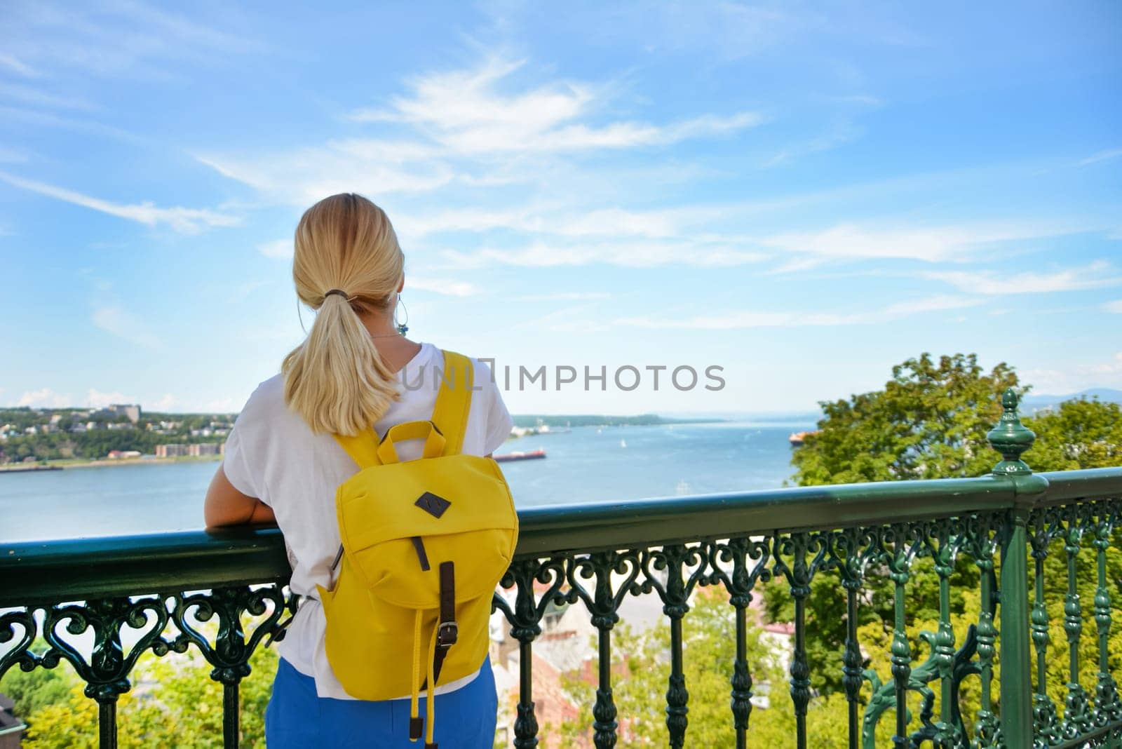 Blond girl with a backpack looking at the river Saint Lawrence at Quebec Canada Sanny day by Chateau Frontenac Castle