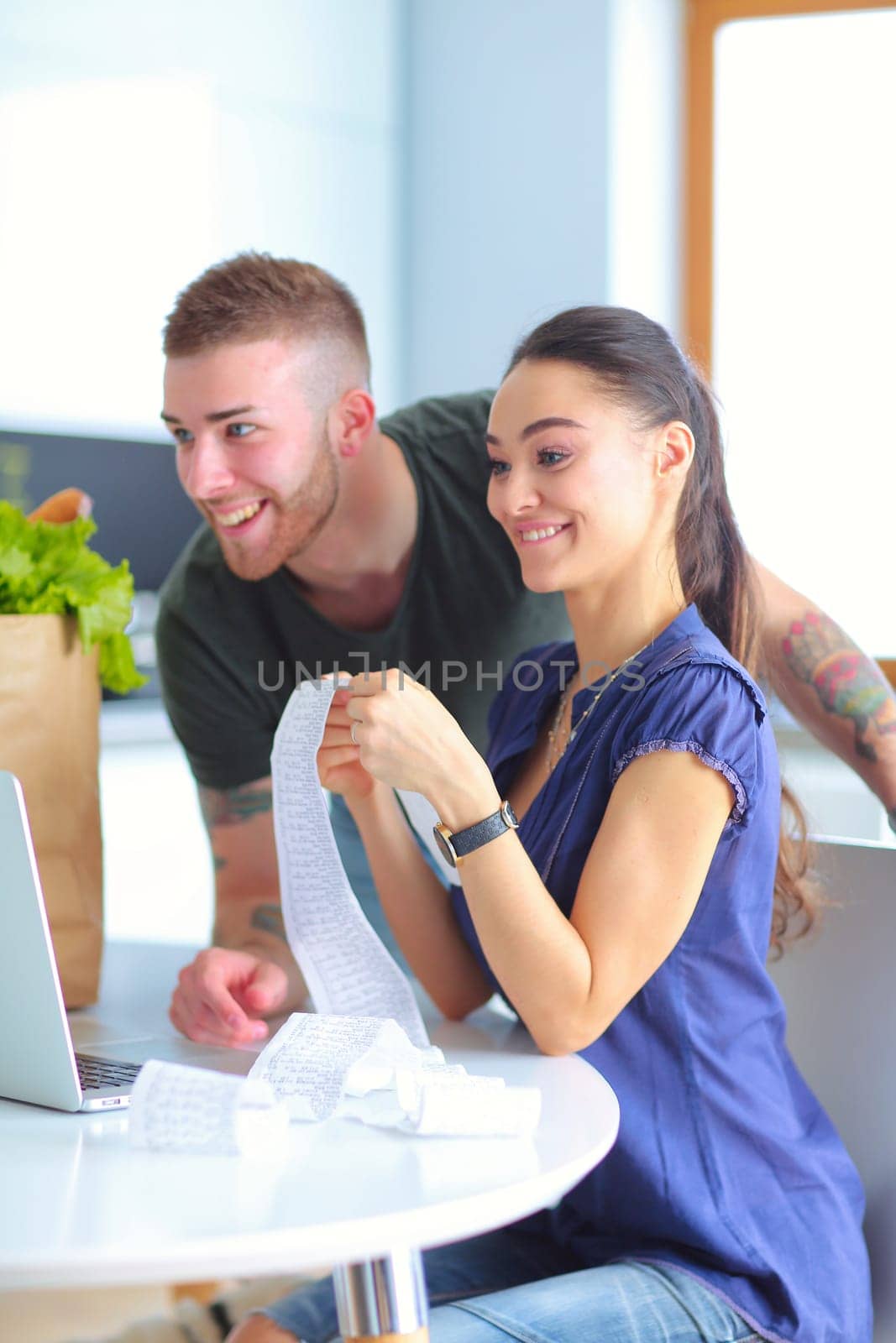 Couple paying their bills with laptop in kitchen at home.