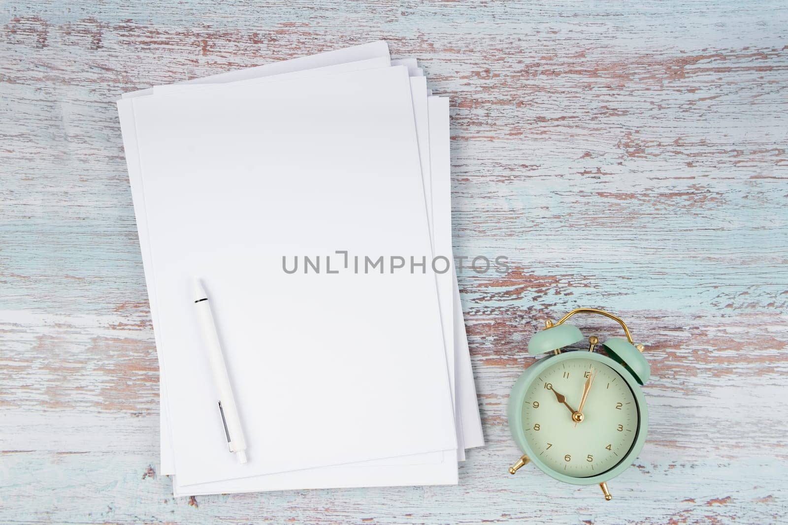 The Top view of heap empty A4 paper and vintage alarm on wooden background for your text or message. by Gamjai