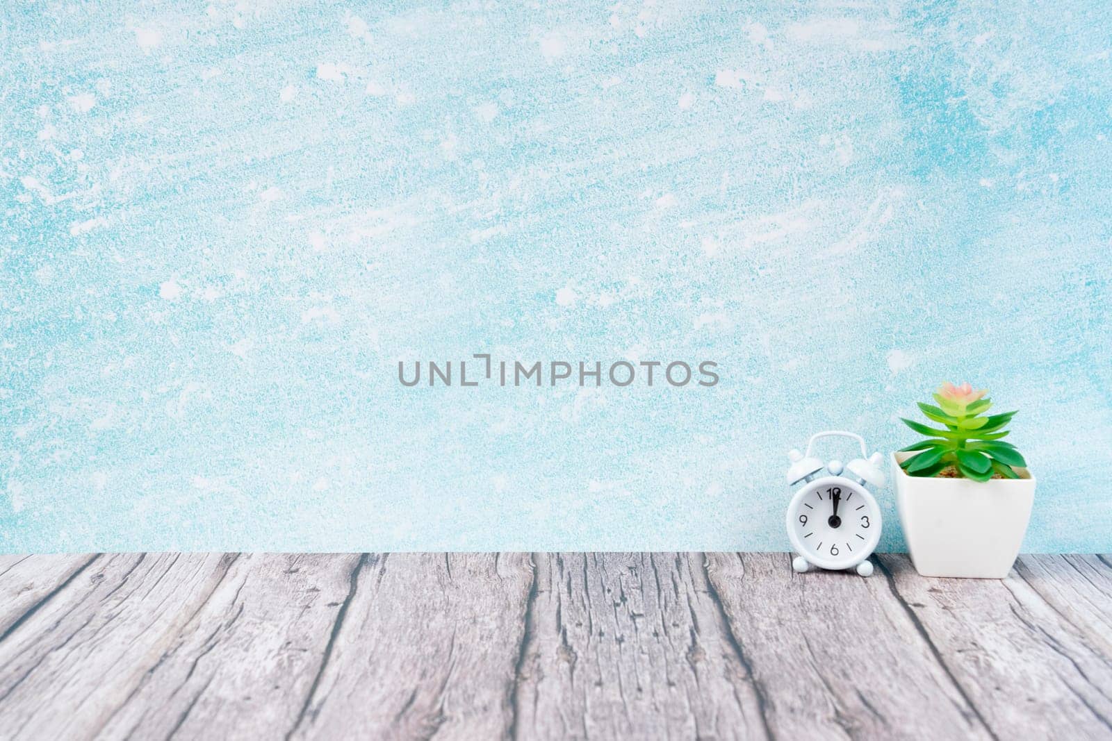 Alarm clock on wood floor and cement wall with plant pot decorate, empty room for background.