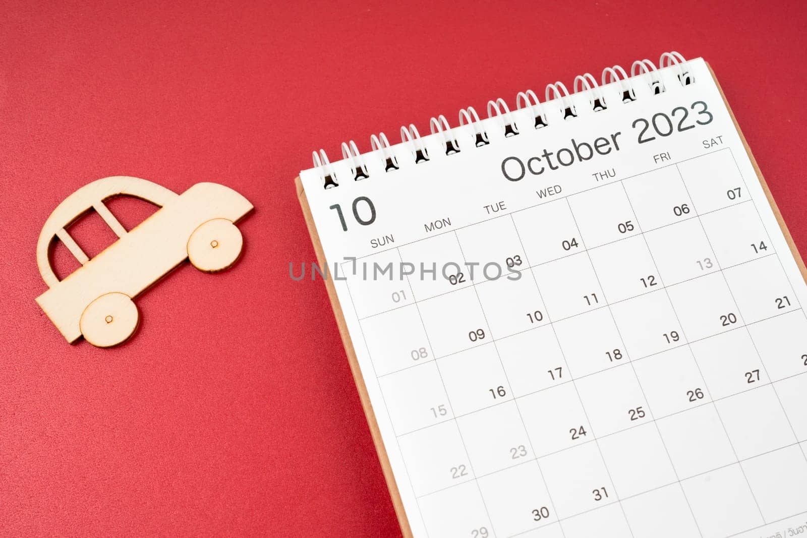 October 2023 desk calendar and wooden toy cars on red background.