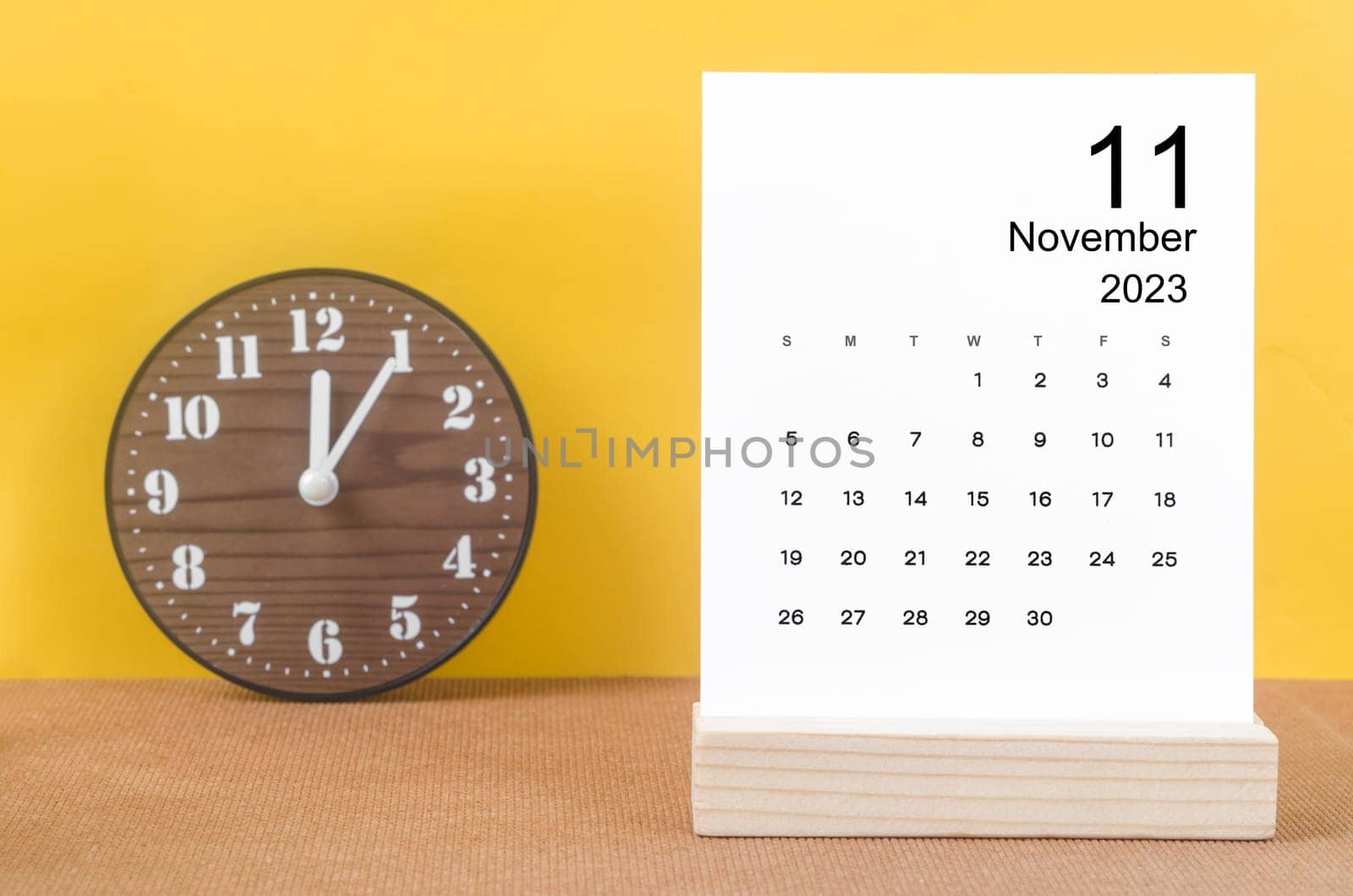 The November 2023 Monthly calendar for 2023 year with clock on yellow table. by Gamjai