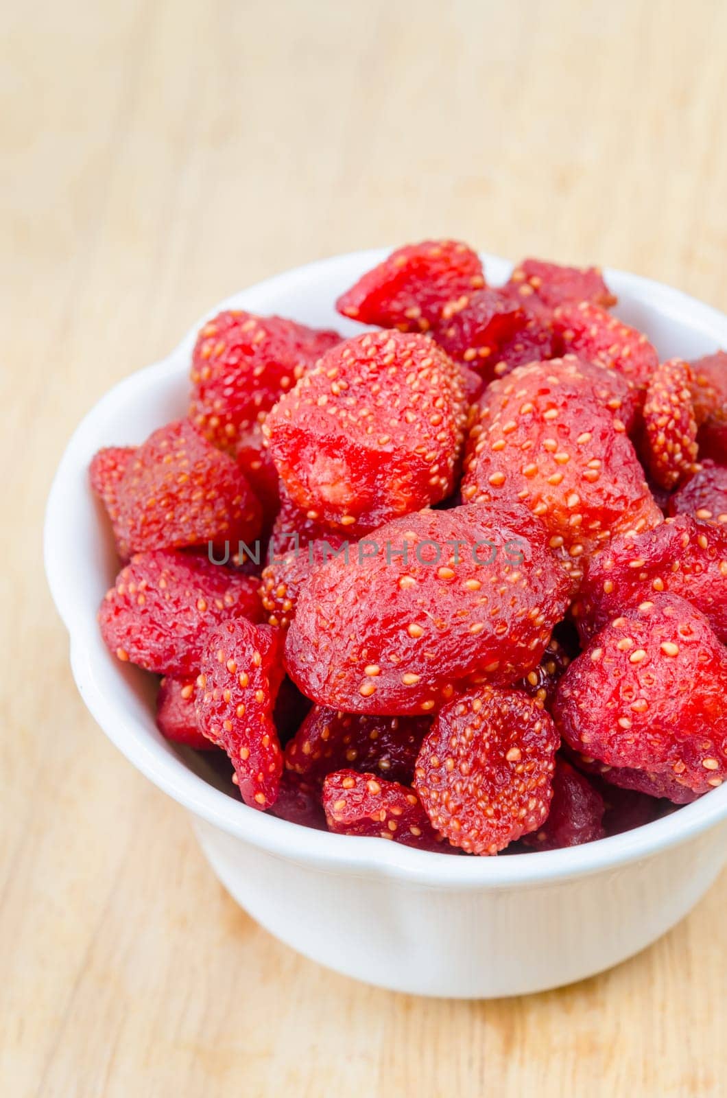 The Close-up Dried Strawberries in white cup on wooden background. by Gamjai