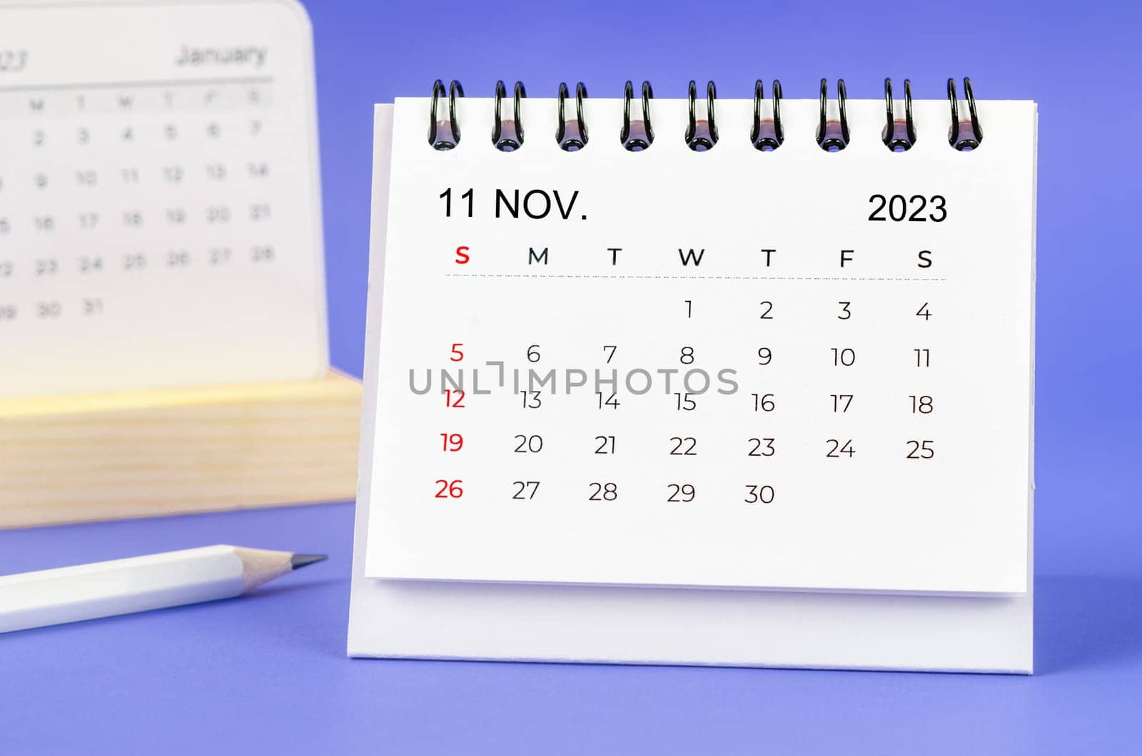 The November 2023 Monthly desk calendar for 2023 year with pencil on purple background. by Gamjai