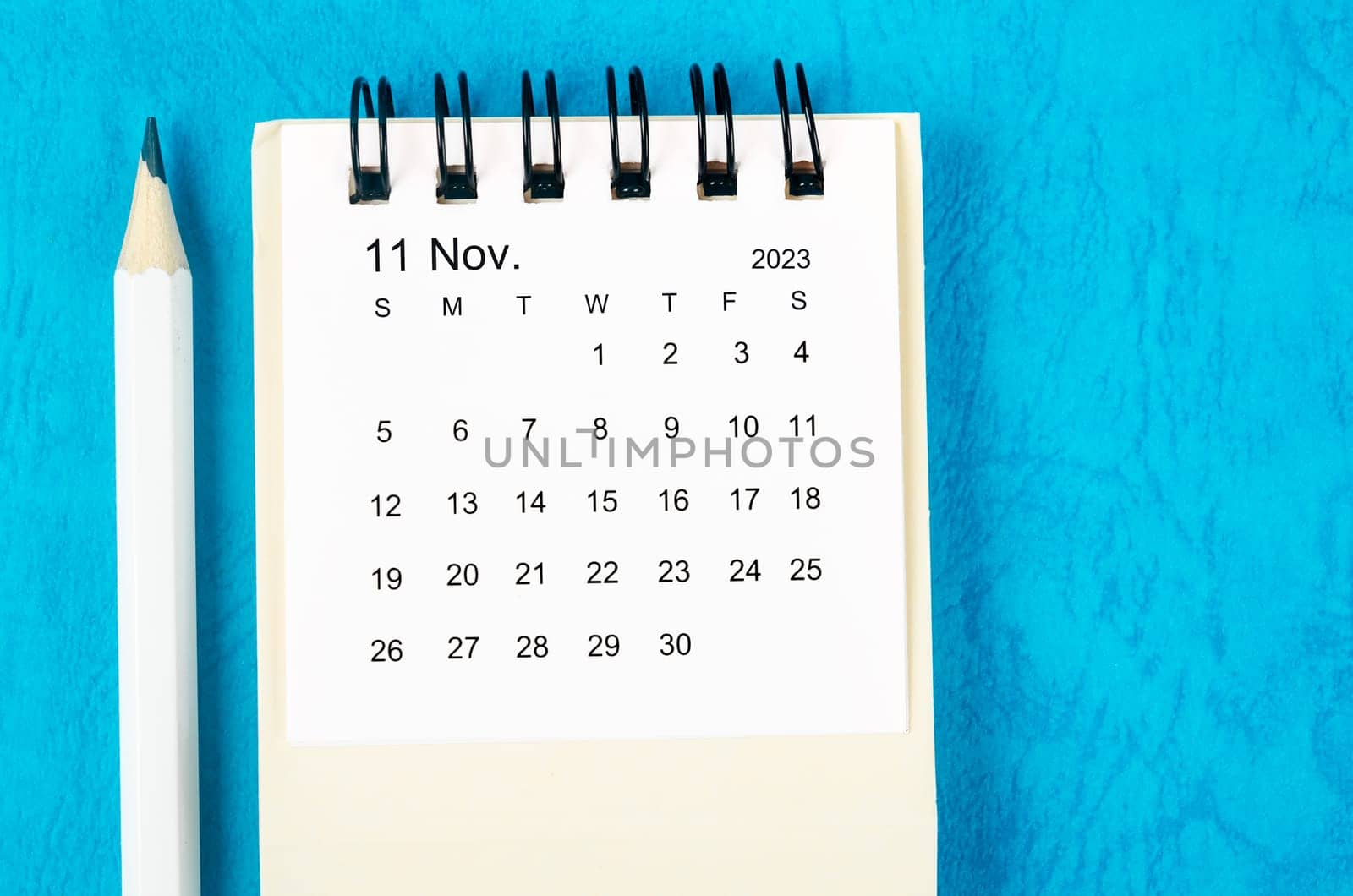 November 2023 Monthly desk calendar for 2023 with pencil on blue background.