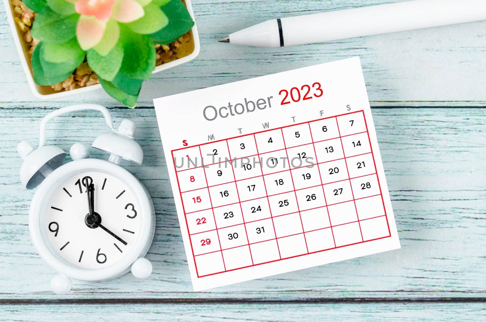 The October 2023 Monthly calendar year and alarm clock with pen on blue wooden background. by Gamjai