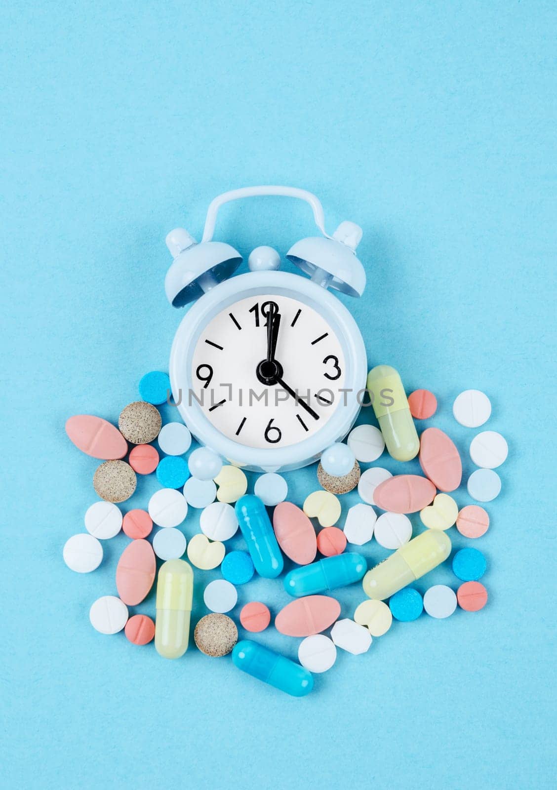 The Medicine time. High angle view of colorful medicines and pills on alarm clock on the blue background. by Gamjai