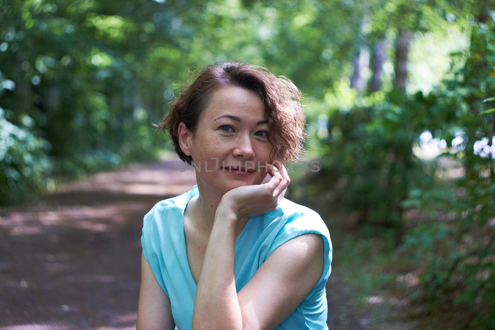 Portrait of a young smiling woman dressed in a blue T-shirt posing for the camera in a park.