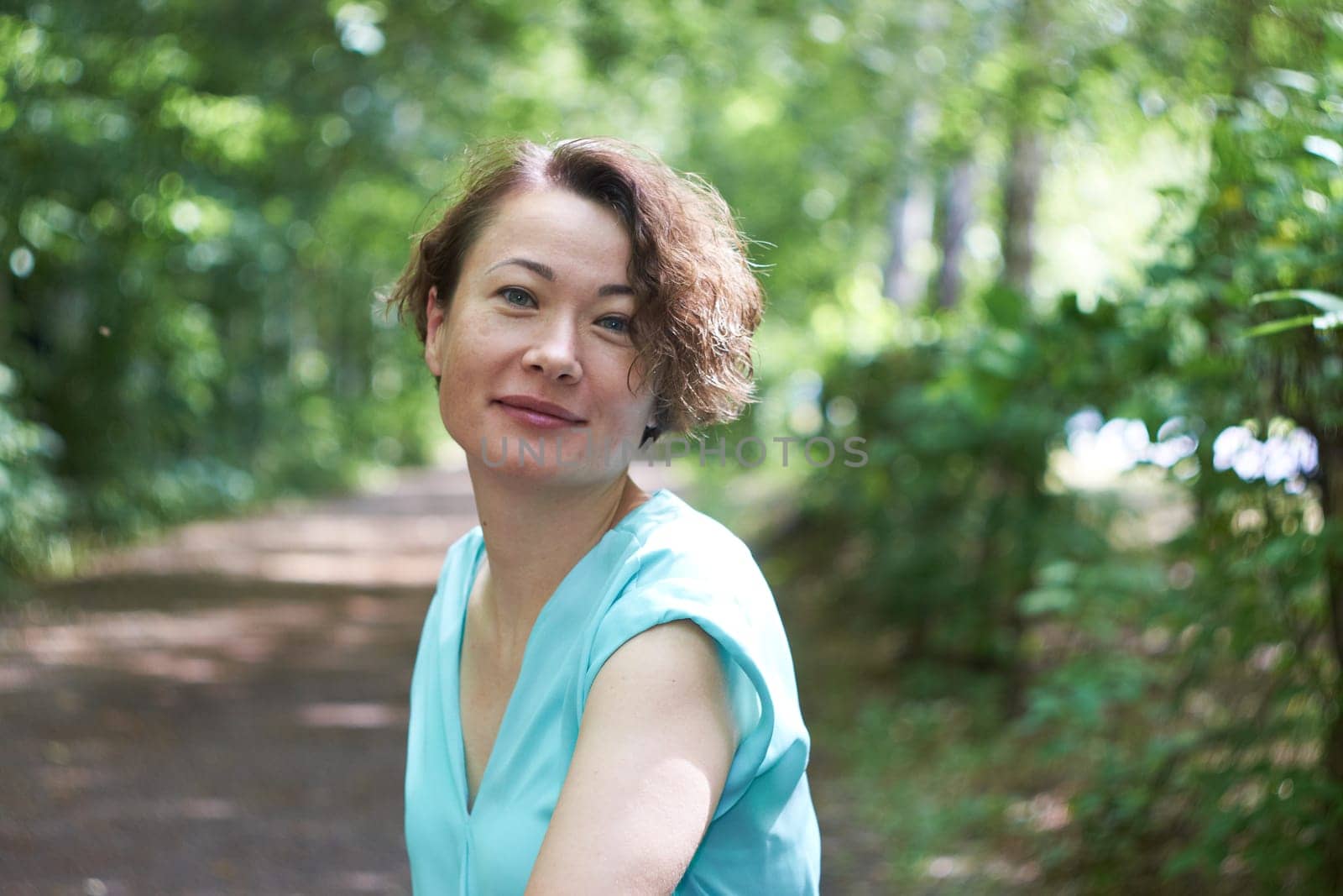 Portrait of a young smiling woman dressed in a blue T-shirt posing for the camera in a park.