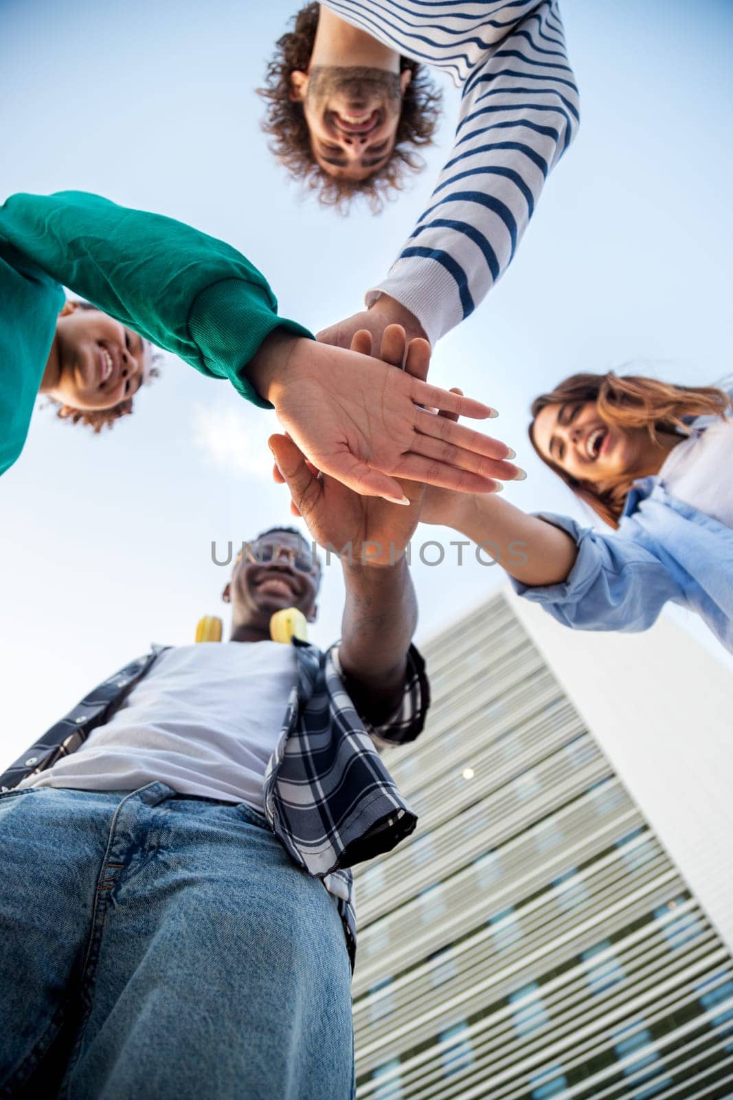 Low angle view of hands piled in the middle. Multiracial friends stacking hands in unity and support. by Hoverstock