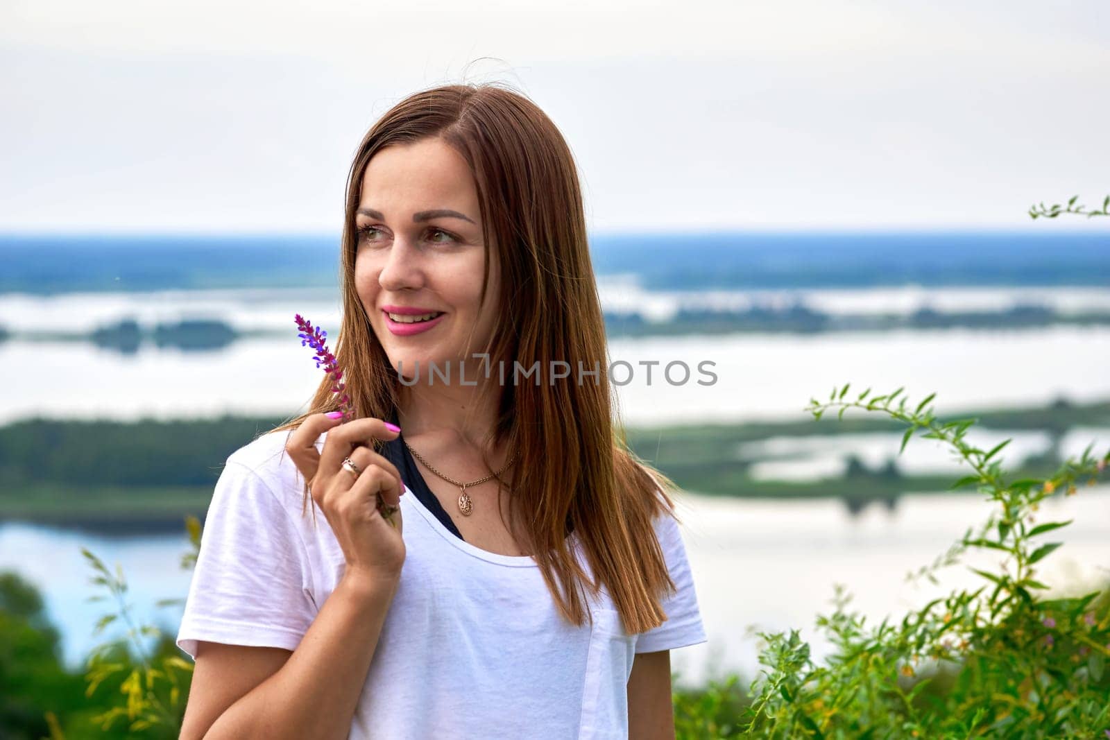 Cute young woman with a flower near the river bank with lush greenery by jovani68