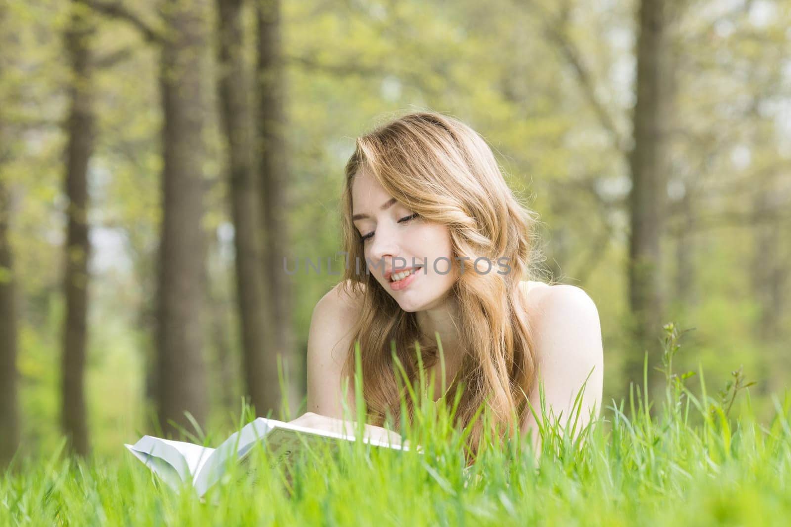 Young beautiful woman lays on green grass field and reads book, spring exam concept, copy space for text