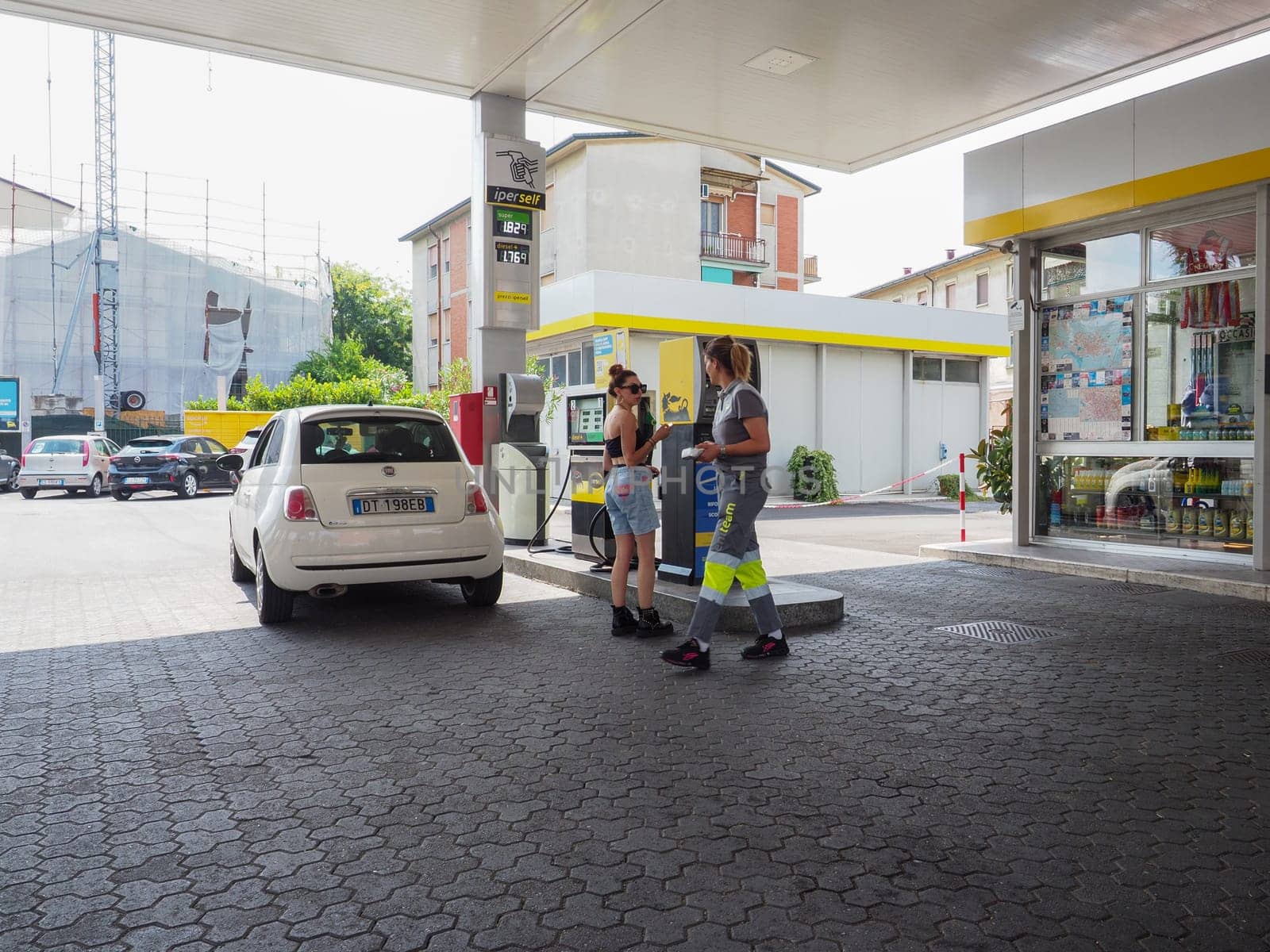 gas station attendant woman taking payments from customers outdoors near fuel pumps by verbano