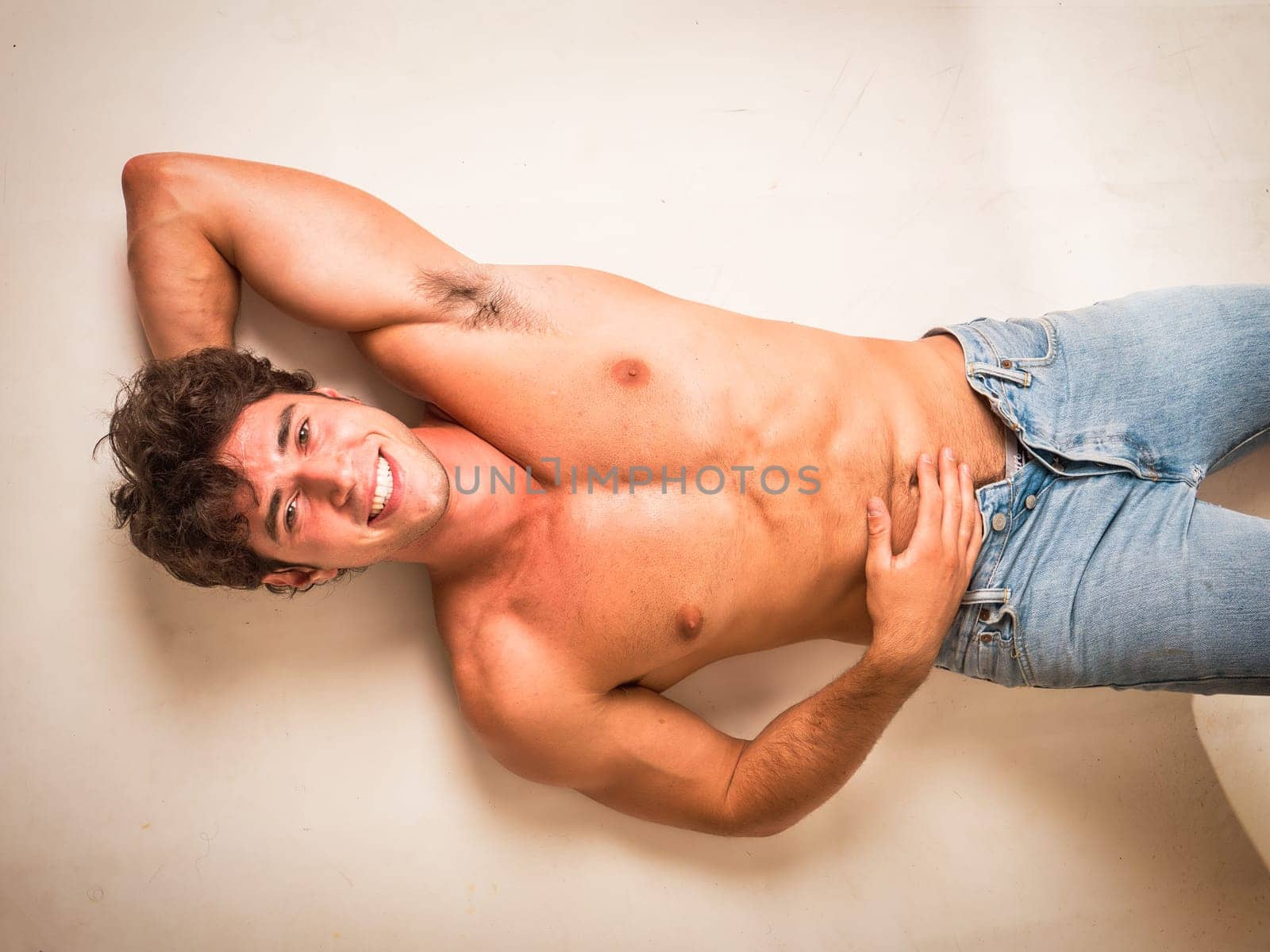 Handsome young bodybuilder laying down on the floor, looking up at the camera with a smile