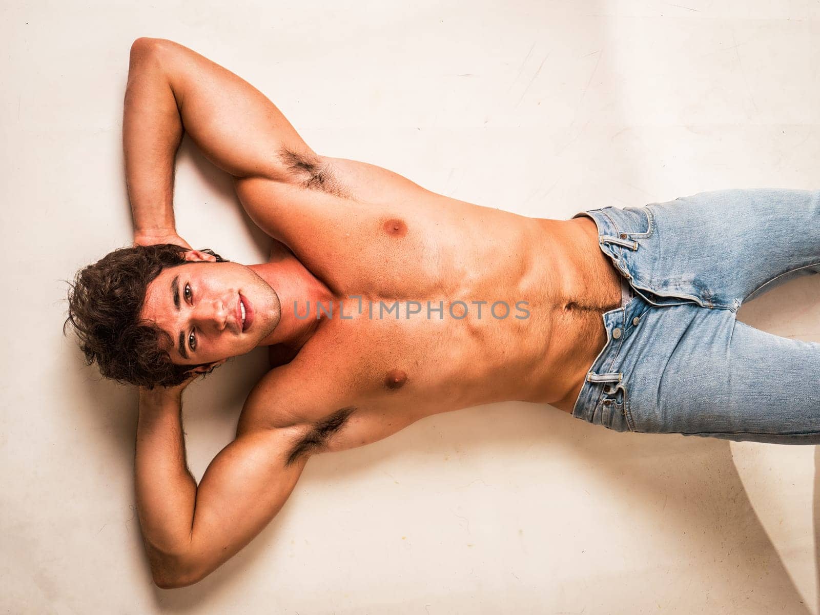 Handsome young bodybuilder laying down on the floor, looking up at the camera with a smile