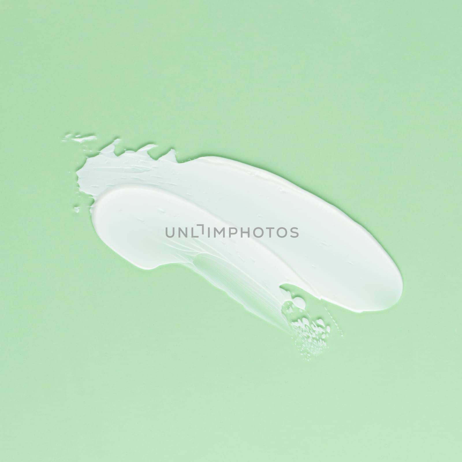 Smear of white cream for face and body on a green background