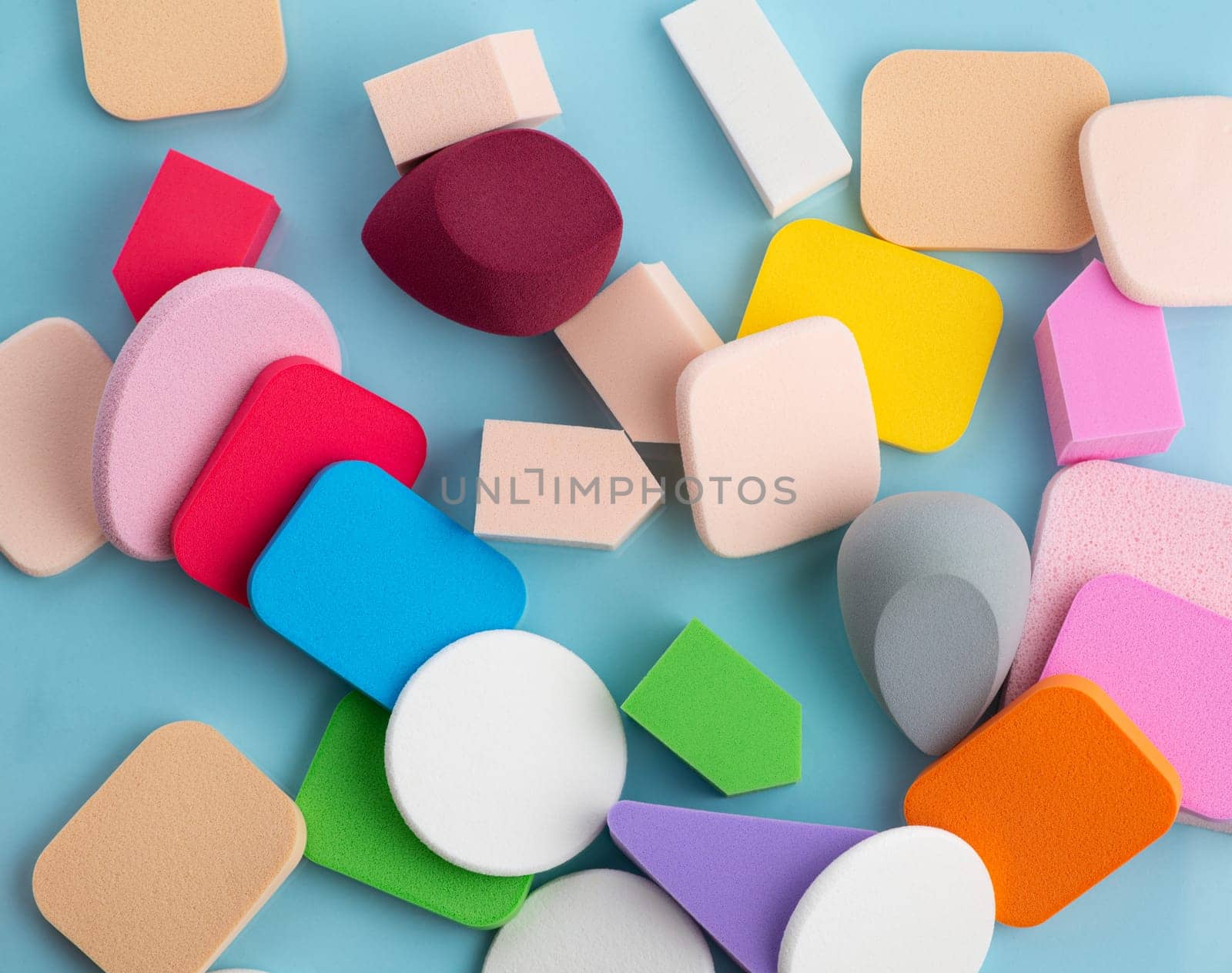 Heap of colorful cosmetic sponges on blue background. Top view by A_Karim