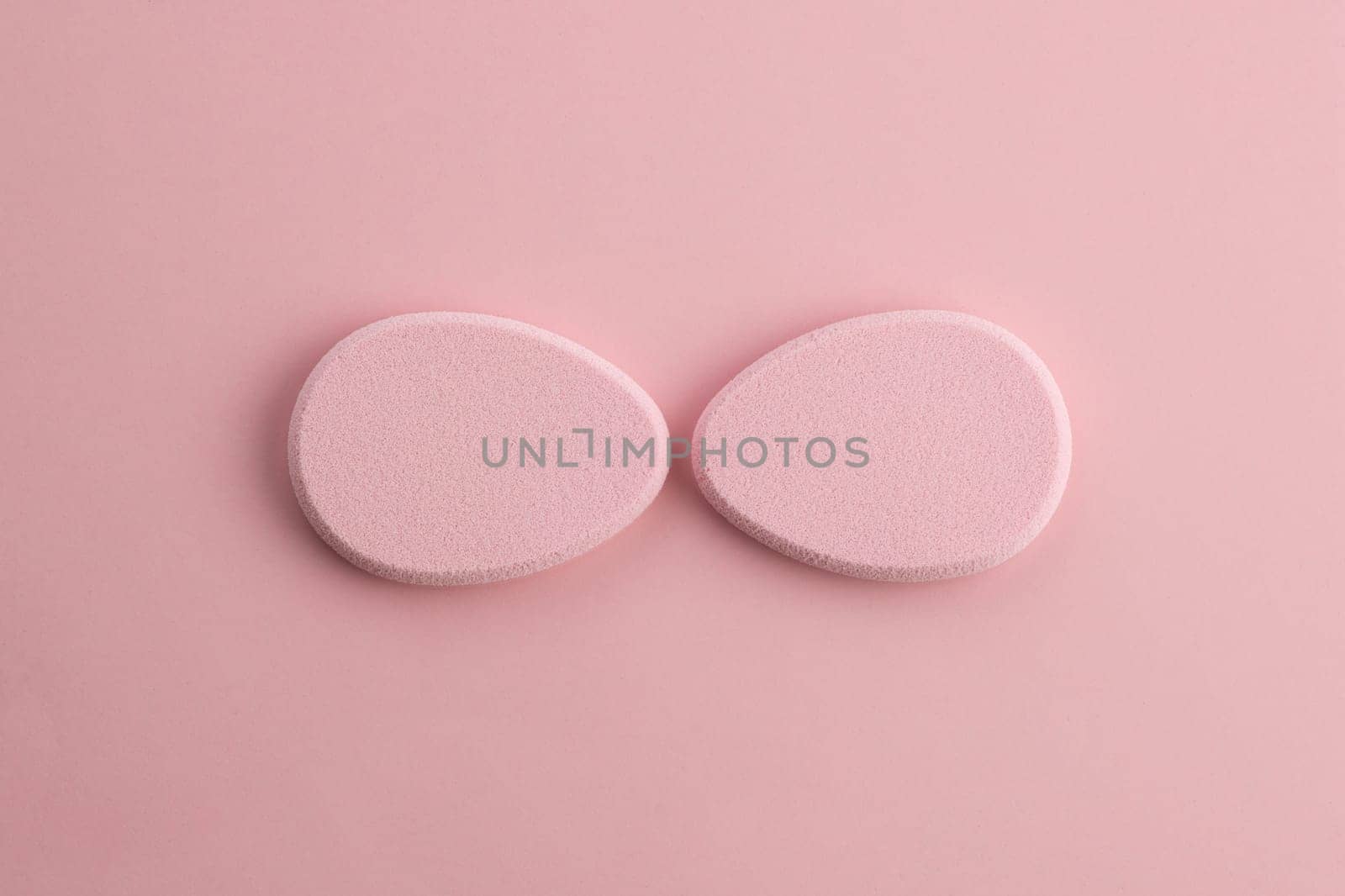 Cosmetic sponge in the shape of an egg on a pink background. Top view