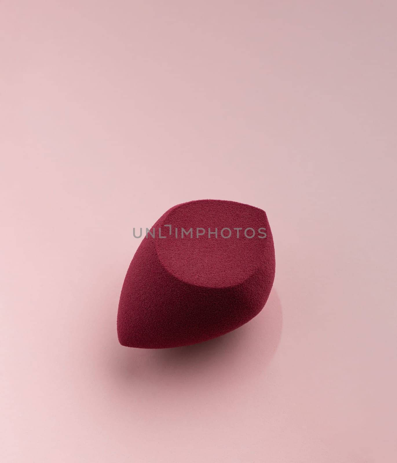 Red cosmetic sponge in the shape of an egg on a pink background by A_Karim