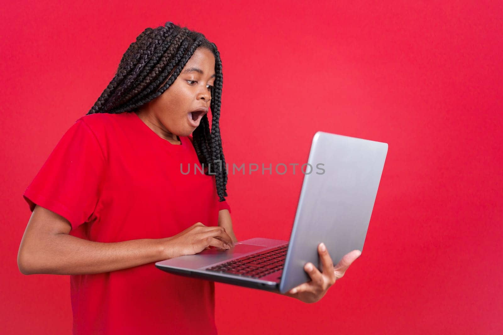 African woman with a surprised look using a laptop in studio with red background