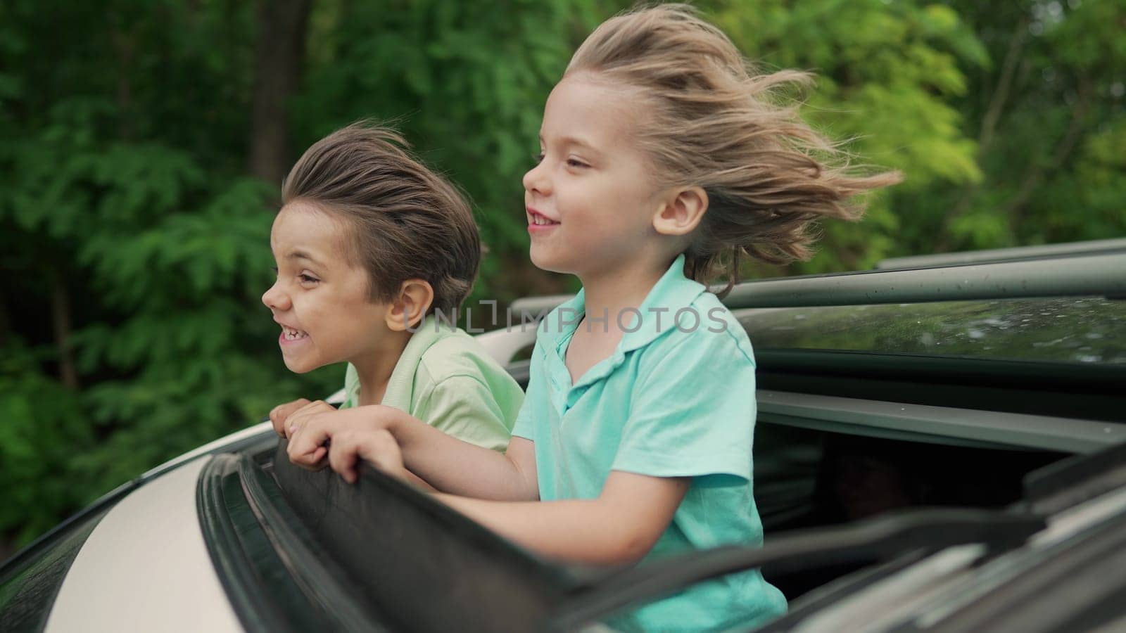 Adorable happy little kids stands in open car sunroof during road trip in countryside at summer. Concept of family leisure, active traveling. High quality