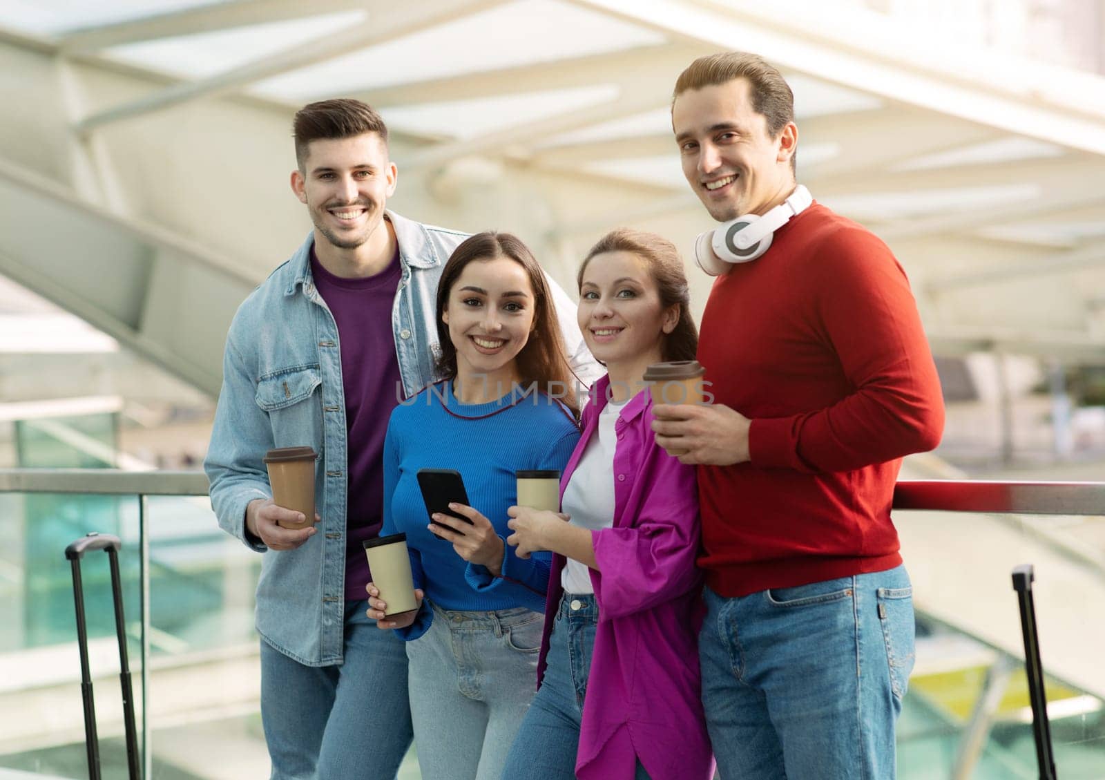 Four Young People Drinking Coffee Before Flight Standing At Departure Terminal In Modern Airport Indoors, Posing With Suitcases Together, Traveling On Vacation With Friends. Transportation Offer