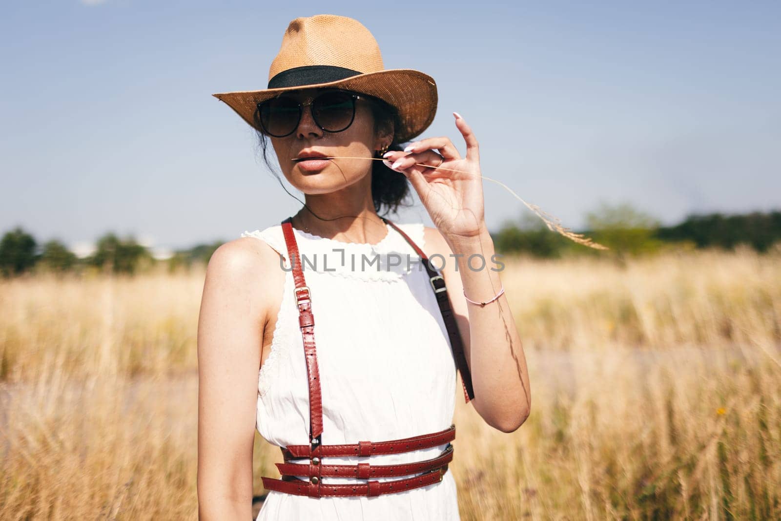 Spirit of freedom. An attractive boho girl in blouse, hat and sunglasses standing on the field on the background of a blue sky. Summer vacation, traveling. Bohemian, modern hippie style. by sarymsakov