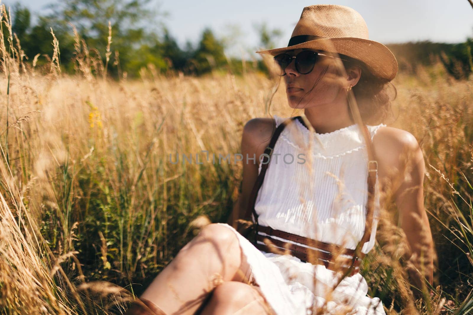 Spirit of freedom. An attractive boho girl in blouse, hat and sunglasses standing on the field on the background of a blue sky. Summer vacation, traveling. Bohemian, modern hippie style