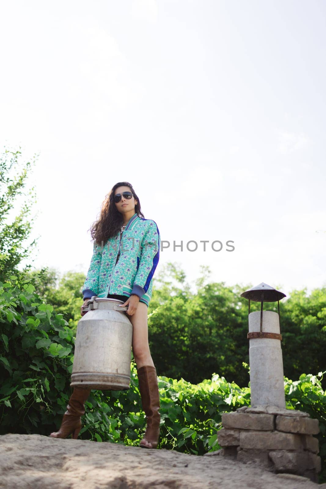 Young fashionable farmer woman posing on camera while holding milk can by sarymsakov