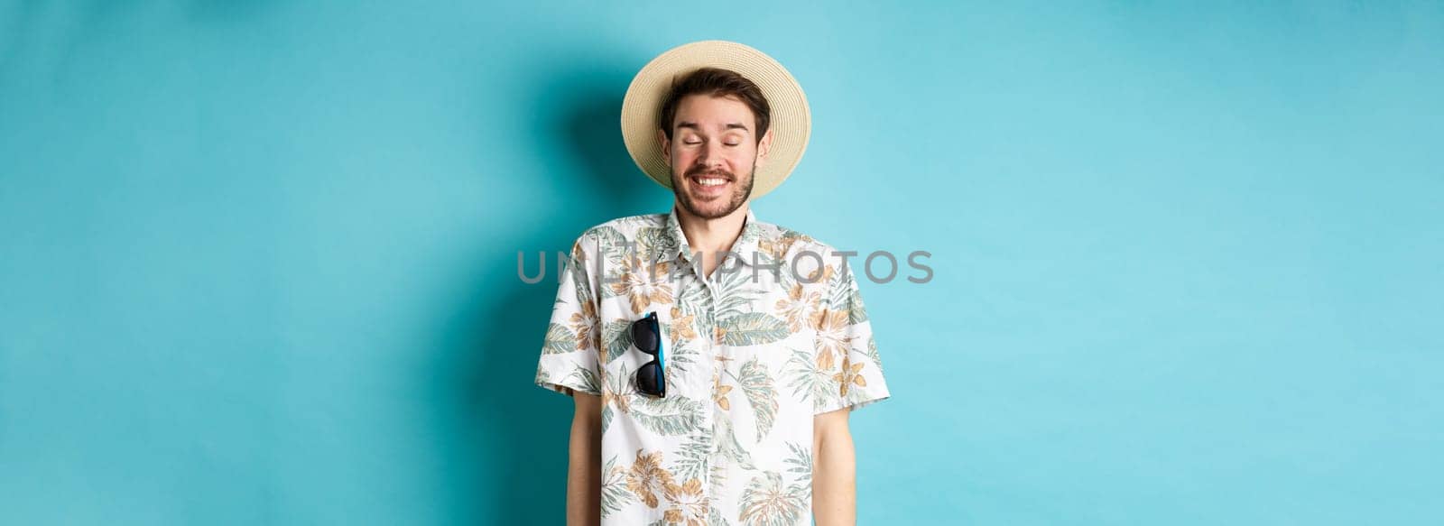 Happy tourist enjoying summer holiday, wearing straw hat and hawaiian shirt, standing joyful on blue background by Benzoix