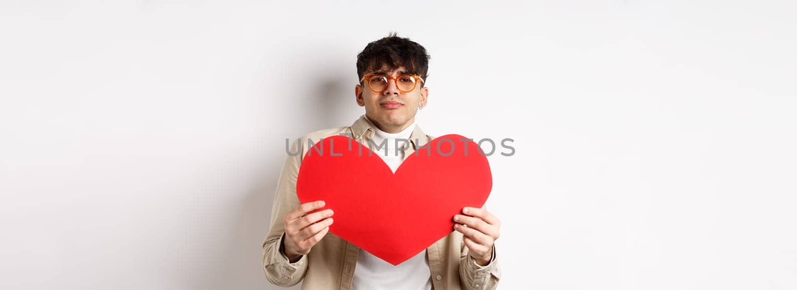 Passionate man waiting for lover with big red heart on Valentines day, looking romantic and with love, standing over white background.