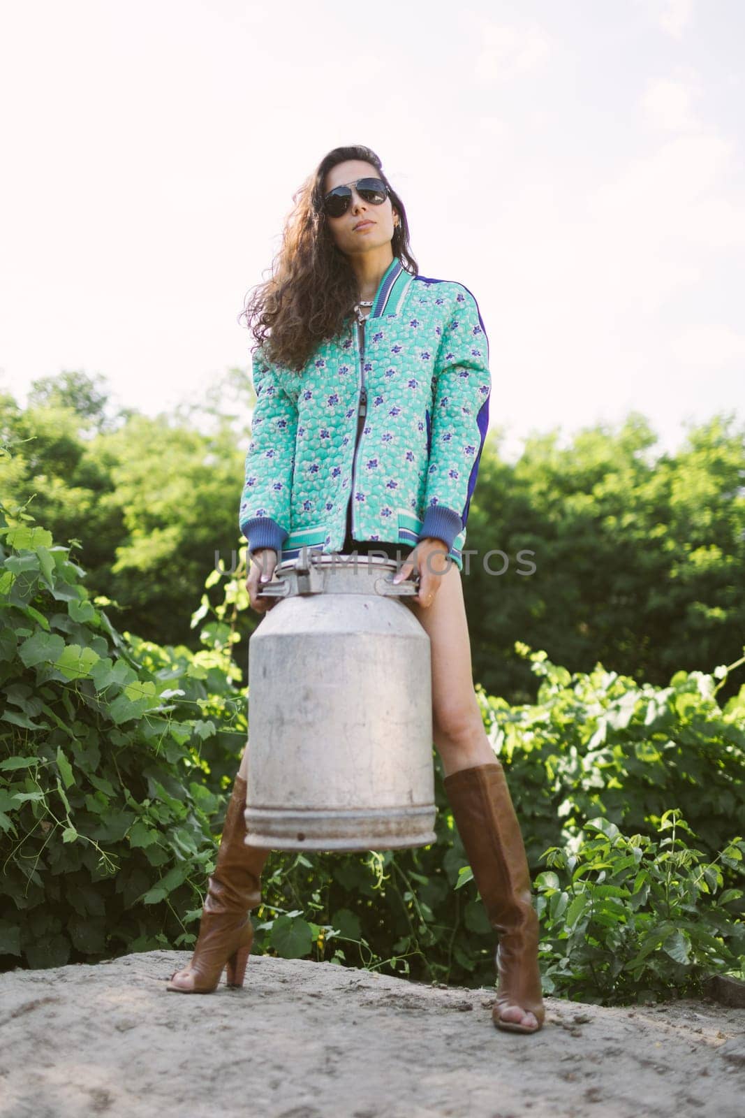 Young fashionable farmer woman posing on camera while holding milk can. by sarymsakov