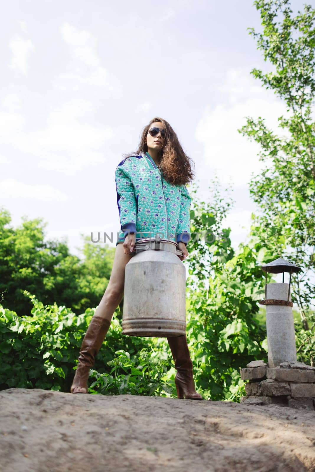 Young fashionable farmer woman posing on camera while holding milk can.