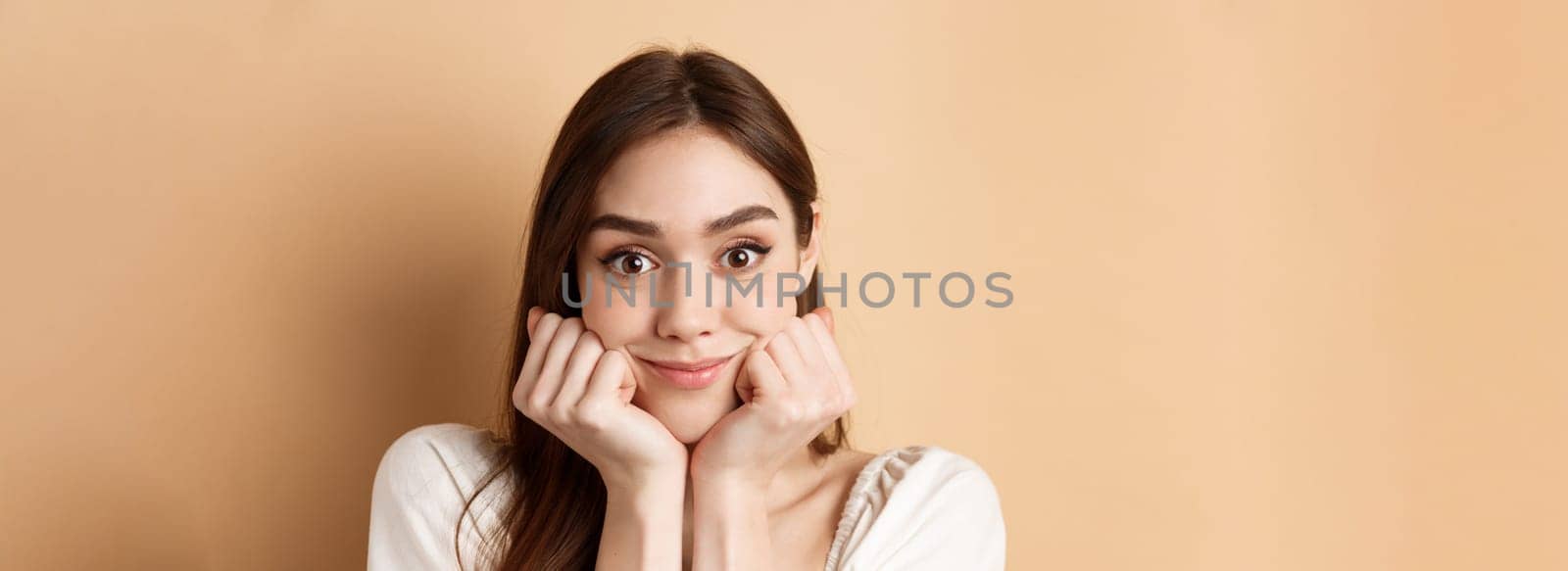 Portrait of intrigued girl listening with interest and excitement, hear interesting story, smiling amused, standing on beige background.